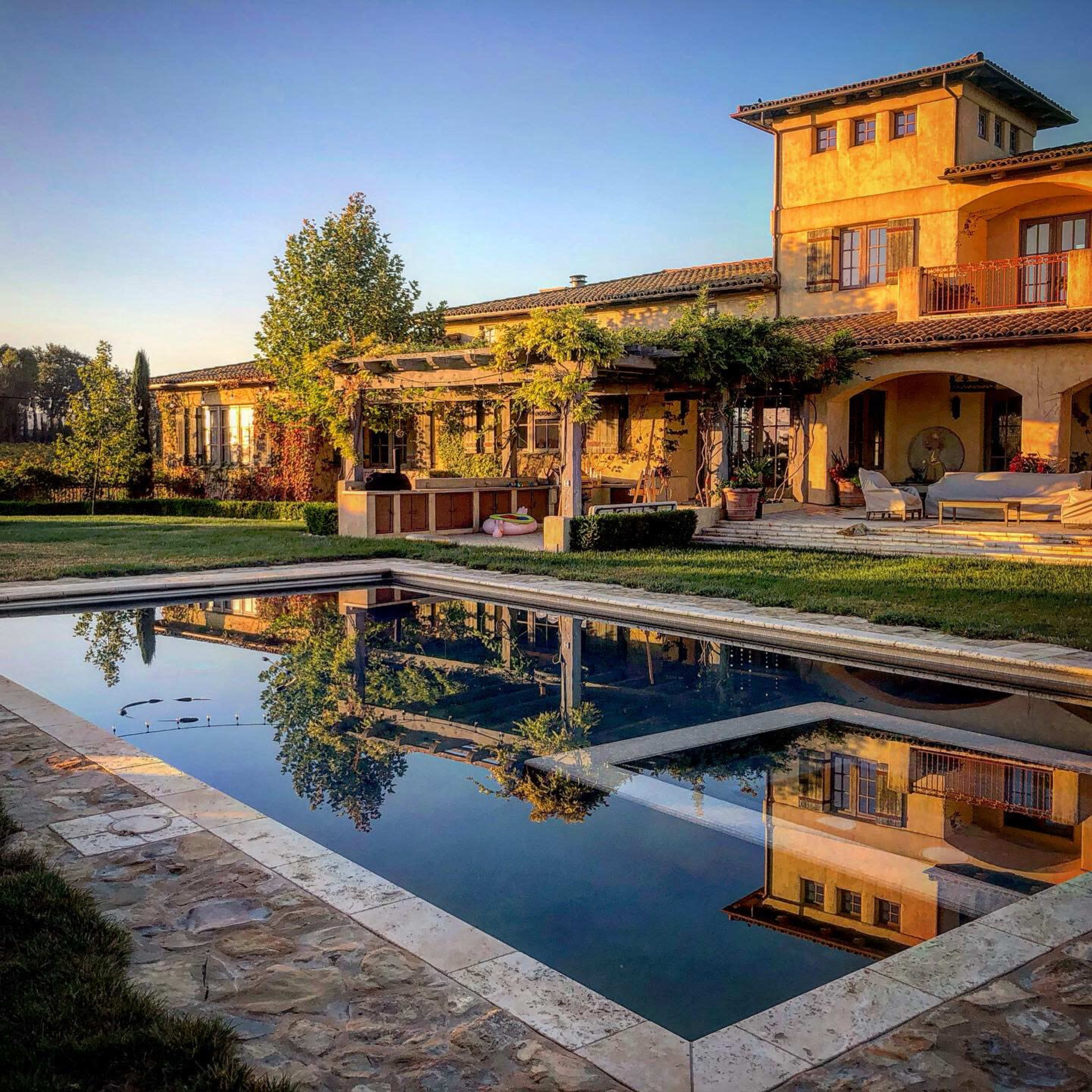 A serene villa with a reflecting pool surrounded by lush greenery and a stone patio.