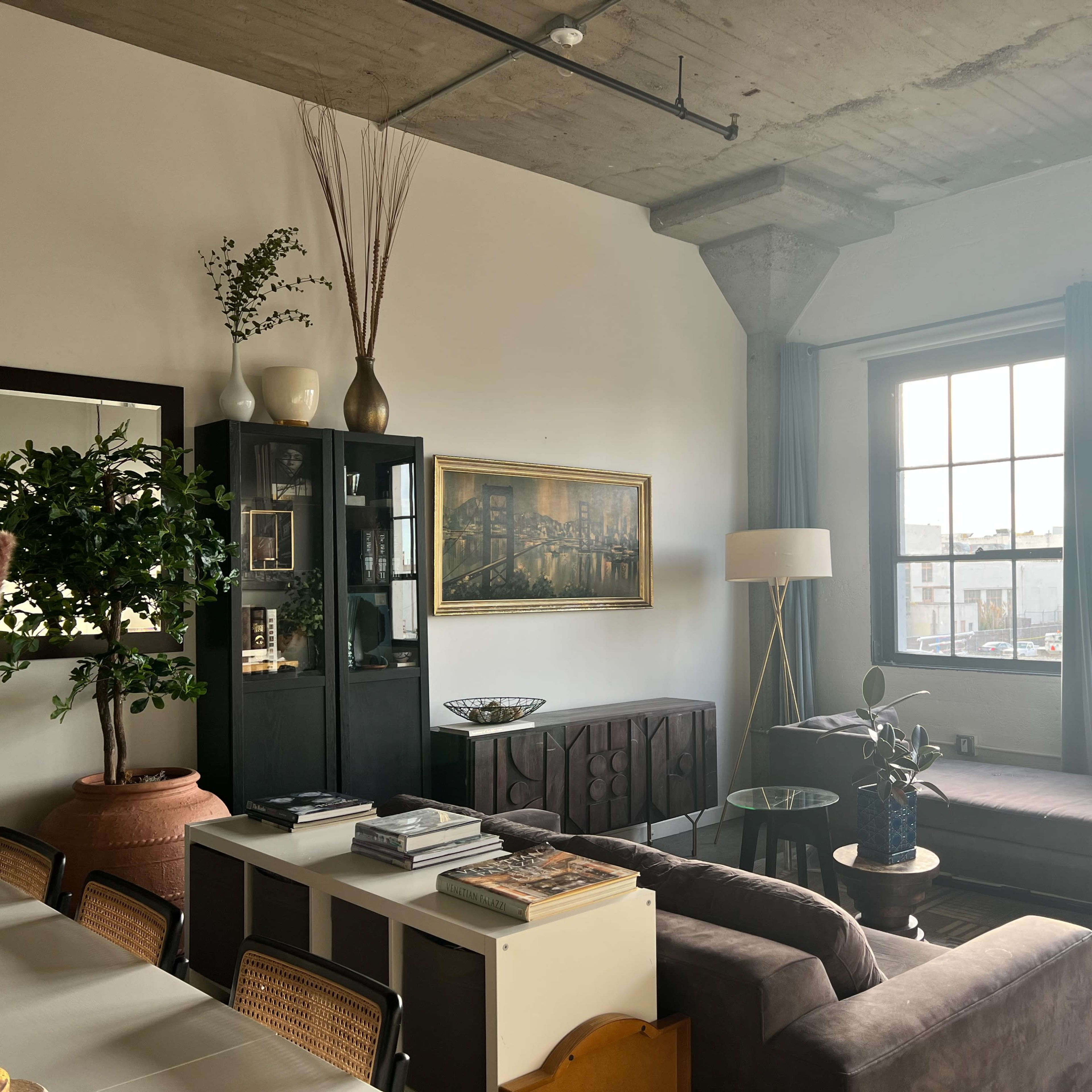 A modern living space with a sofa, coffee table, bookshelves, and large windows allowing natural light to fill the room.
