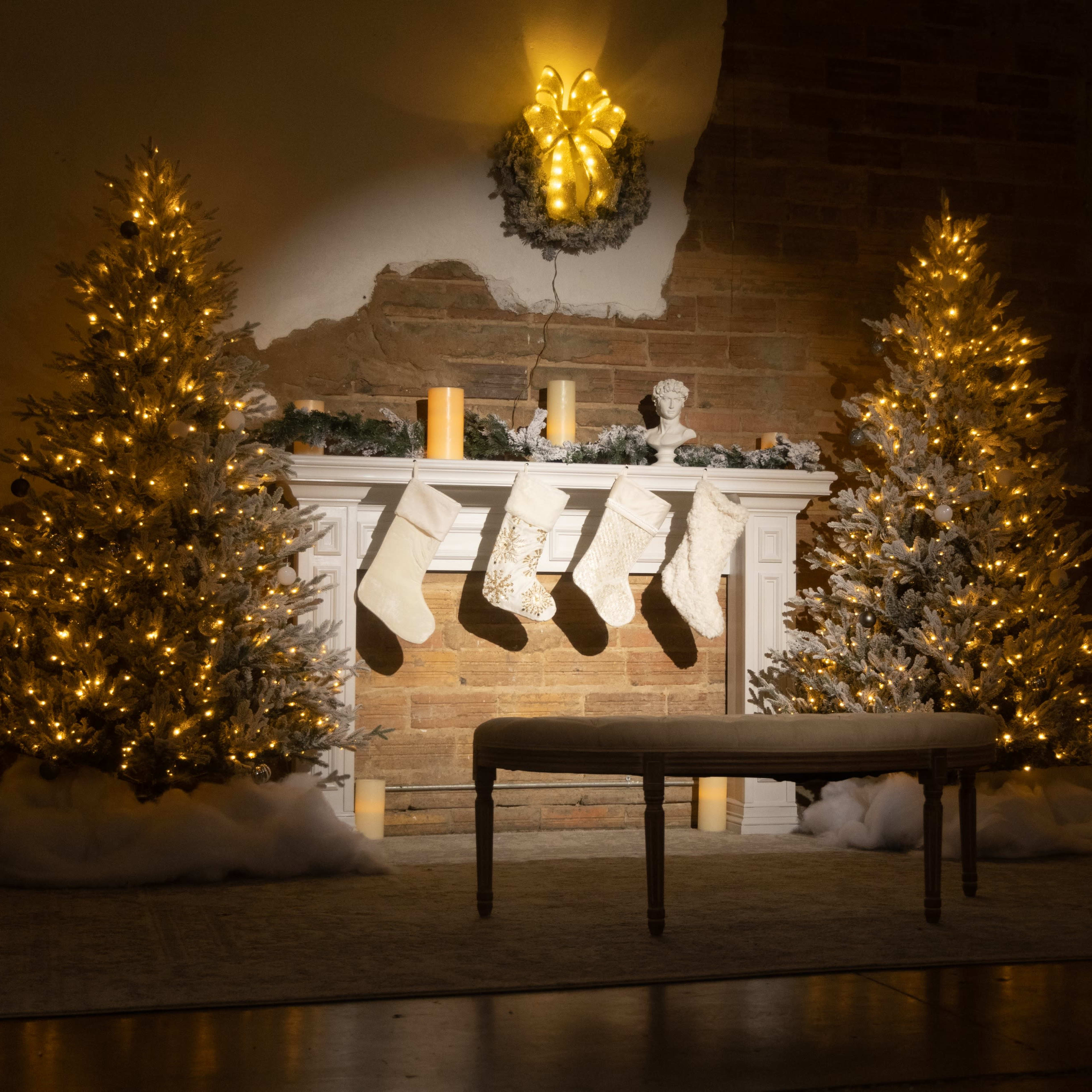 The scene features a decorated fireplace with two illuminated Christmas trees, stockings hung above, and a bench in front.