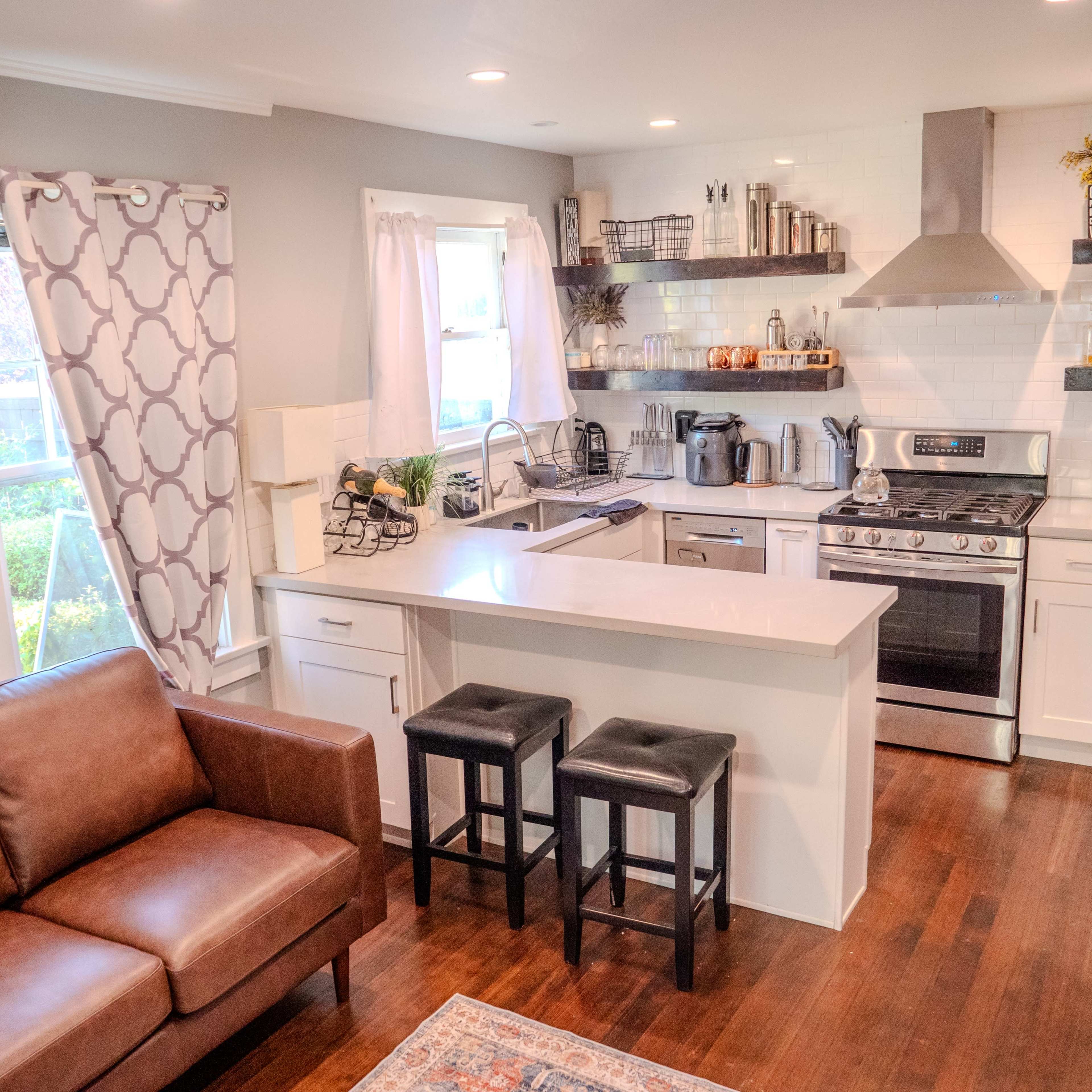 A modern kitchen with a countertop island, stainless steel appliances, a gas stove, and a brown leather couch in the living area.