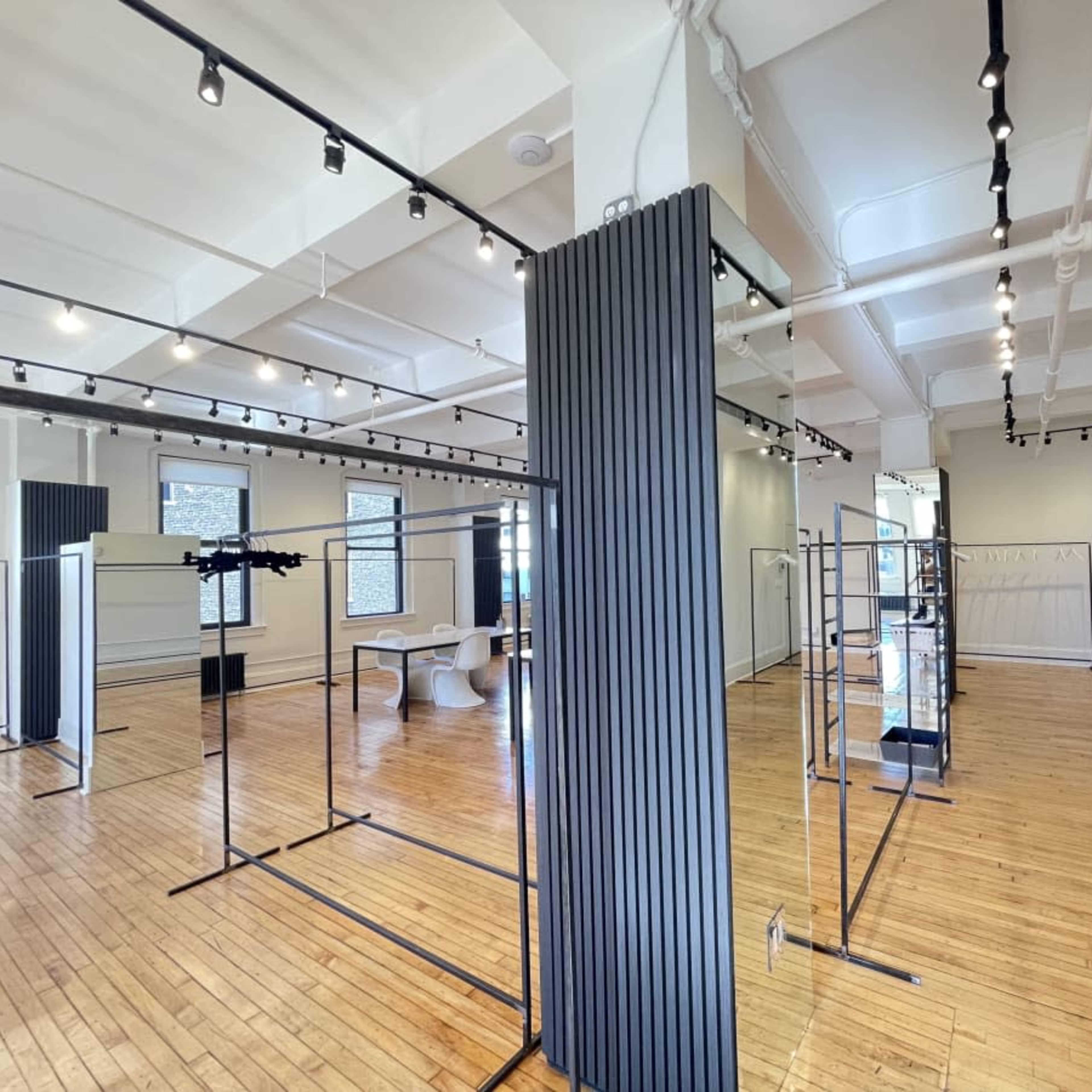 An empty indoor space featuring wooden floors, minimalistic clothing racks, and modern lighting fixtures.