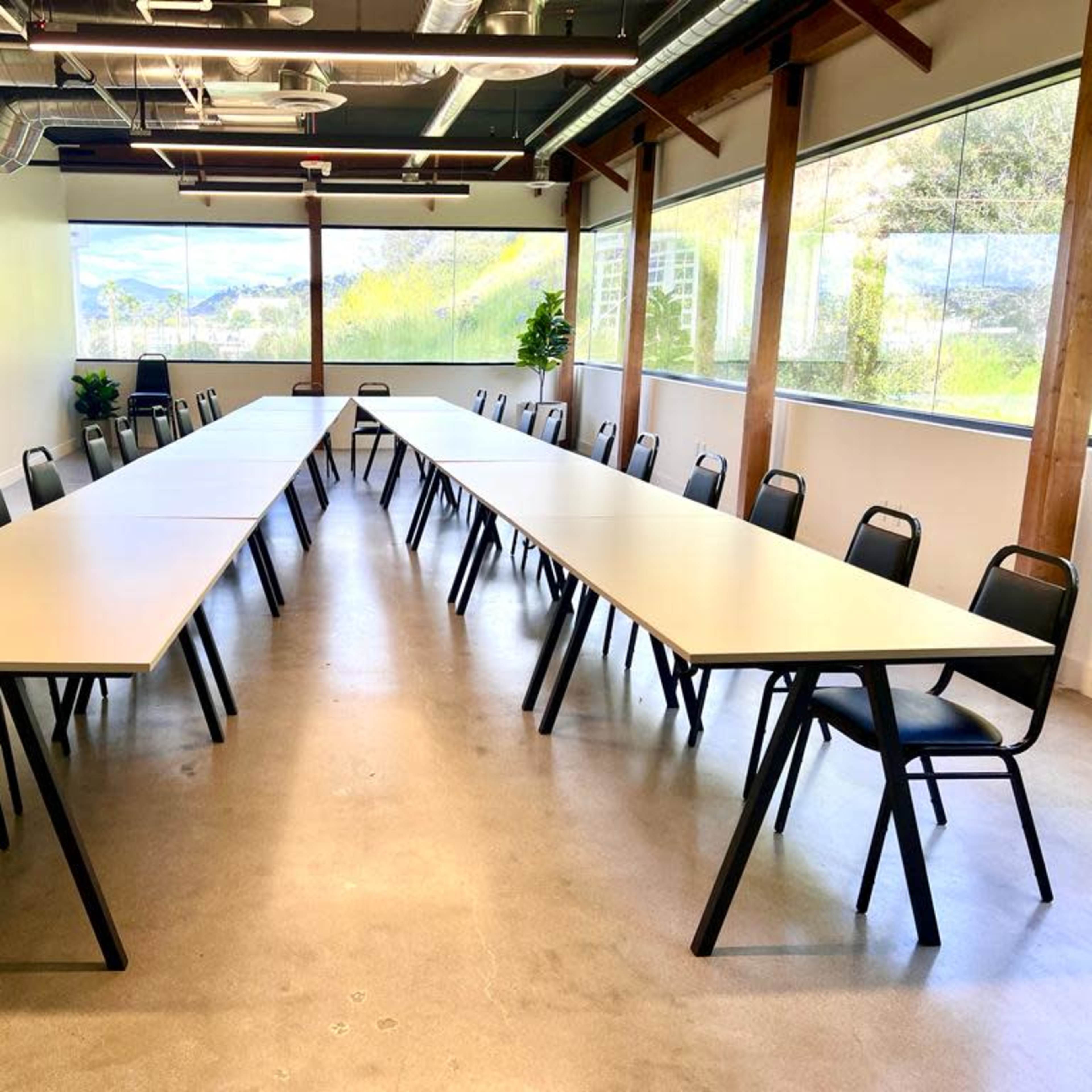A large meeting room with two long tables arranged in a U-shape and black chairs positioned around them.
