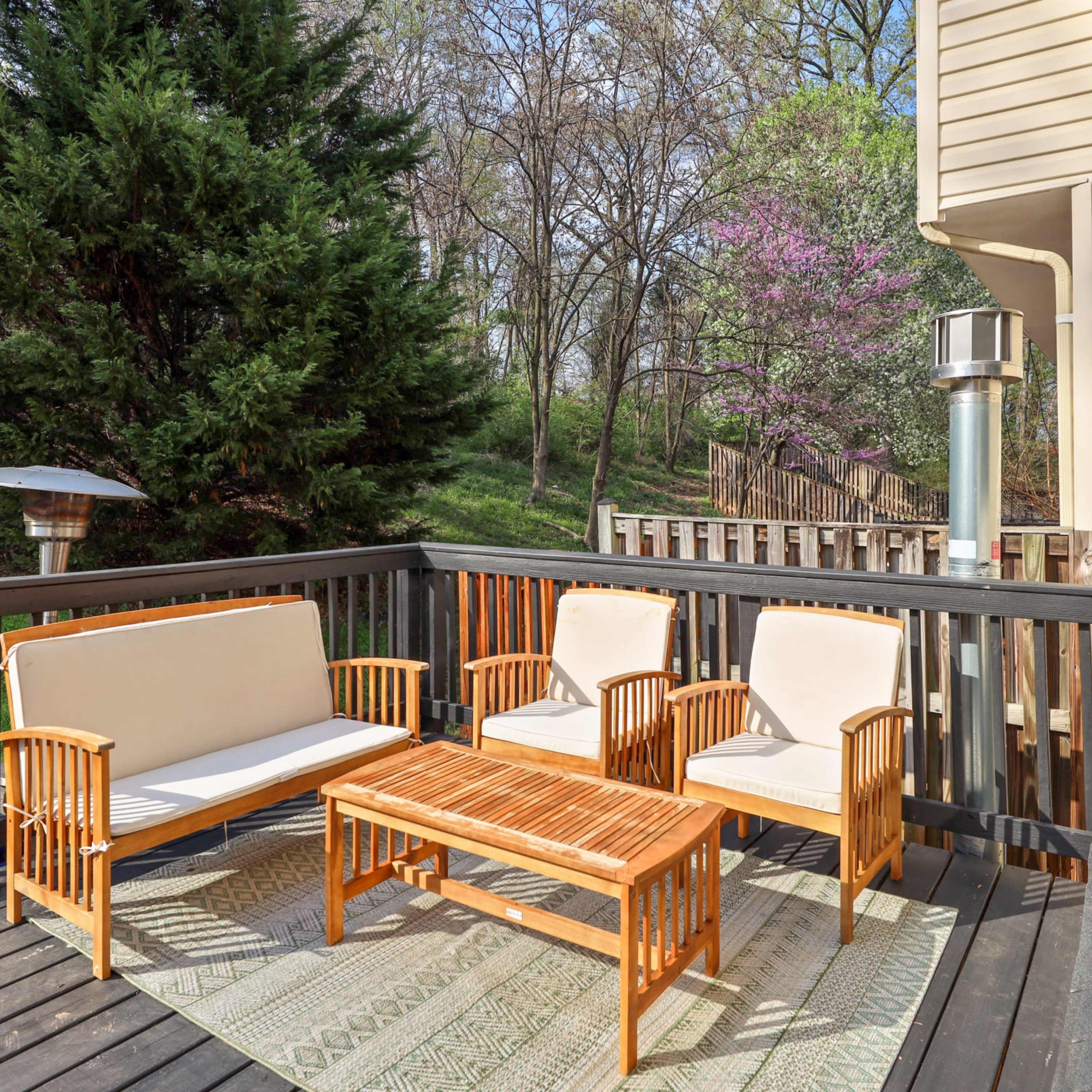 A wooden deck features a seating area with two chairs and a sofa around a coffee table, surrounded by greenery.