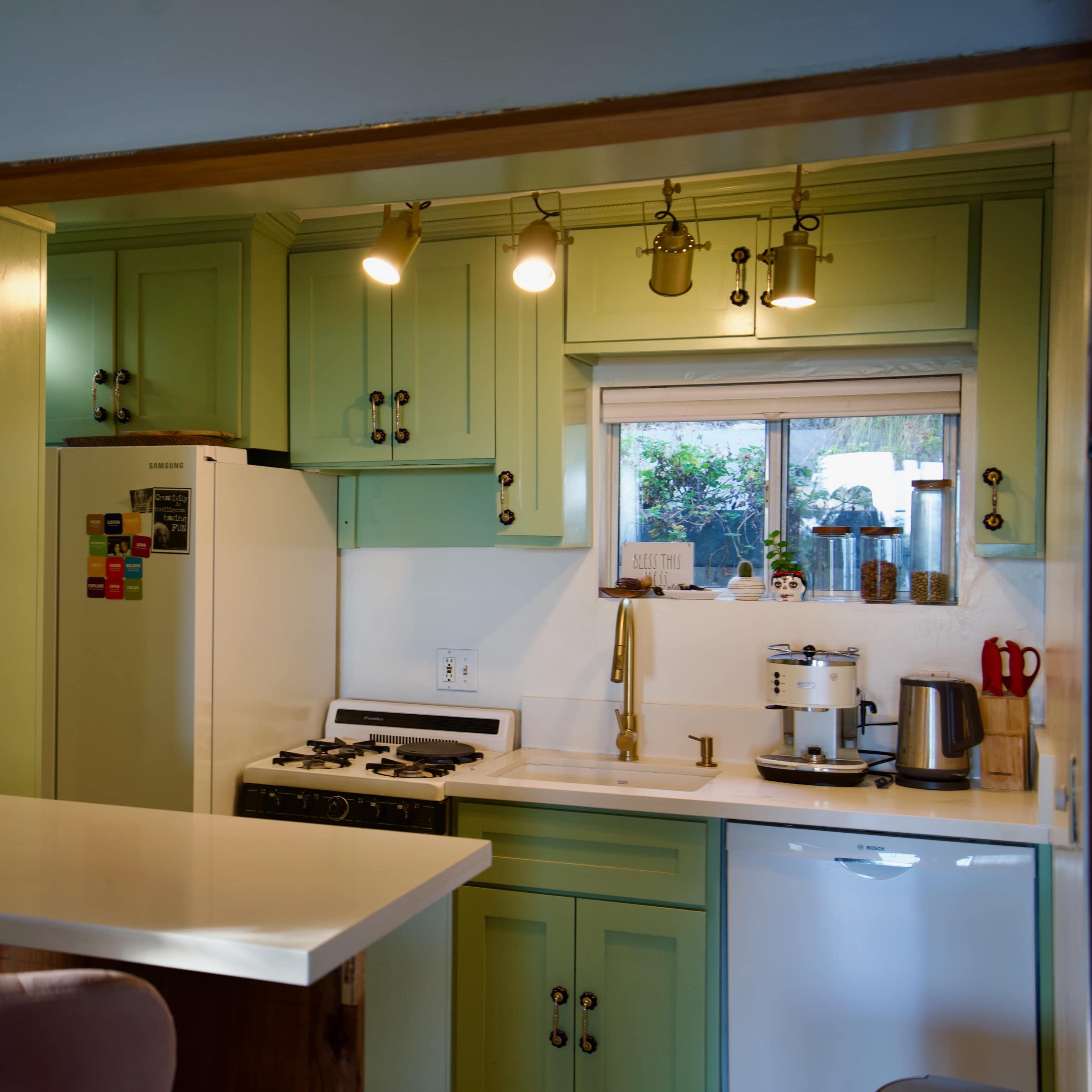 A kitchen with light green cabinets, a white countertop, and stainless steel appliances, including a stove and refrigerator.