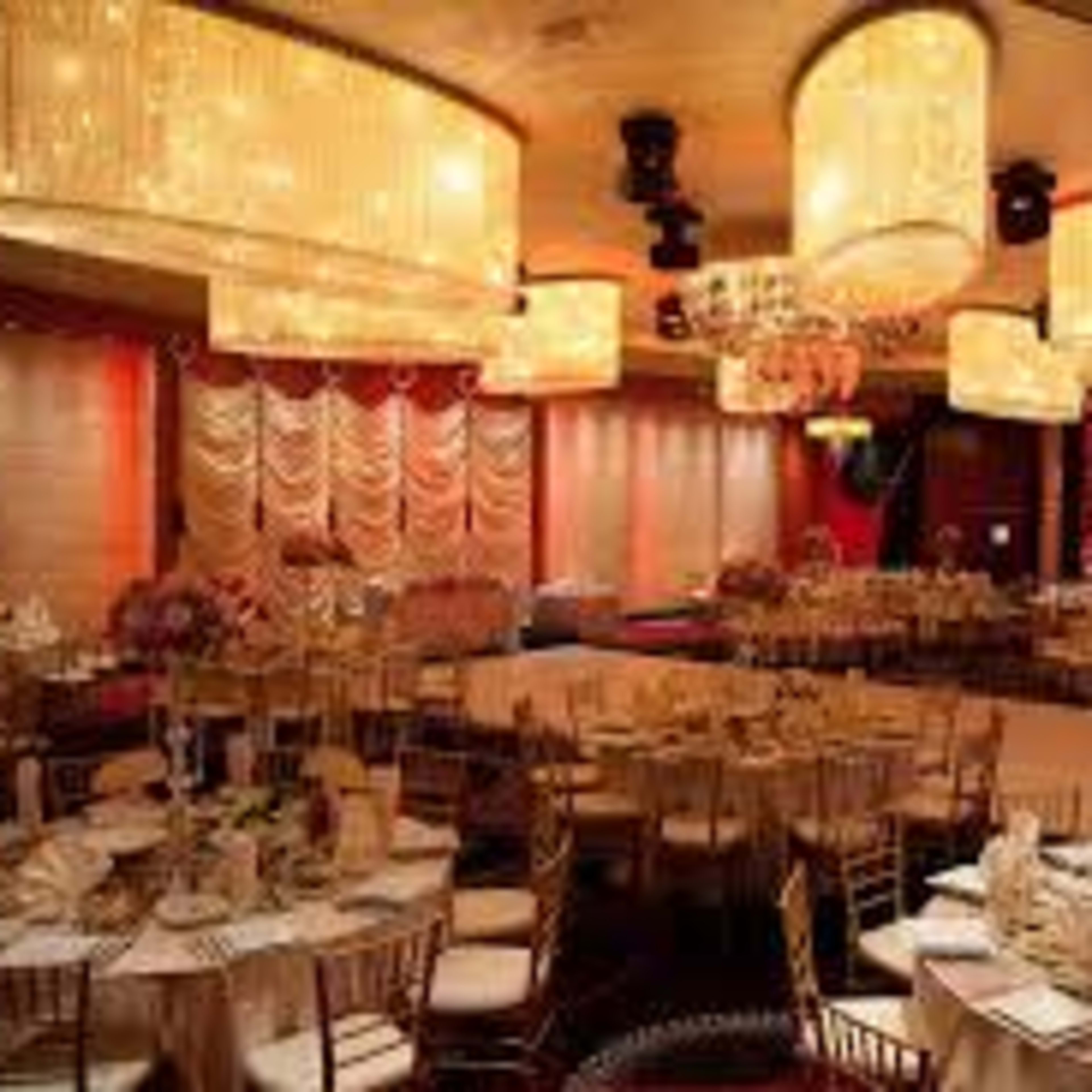 An elegantly arranged banquet hall with round tables set for dining, adorned with floral centerpieces, and illuminated by large chandeliers.