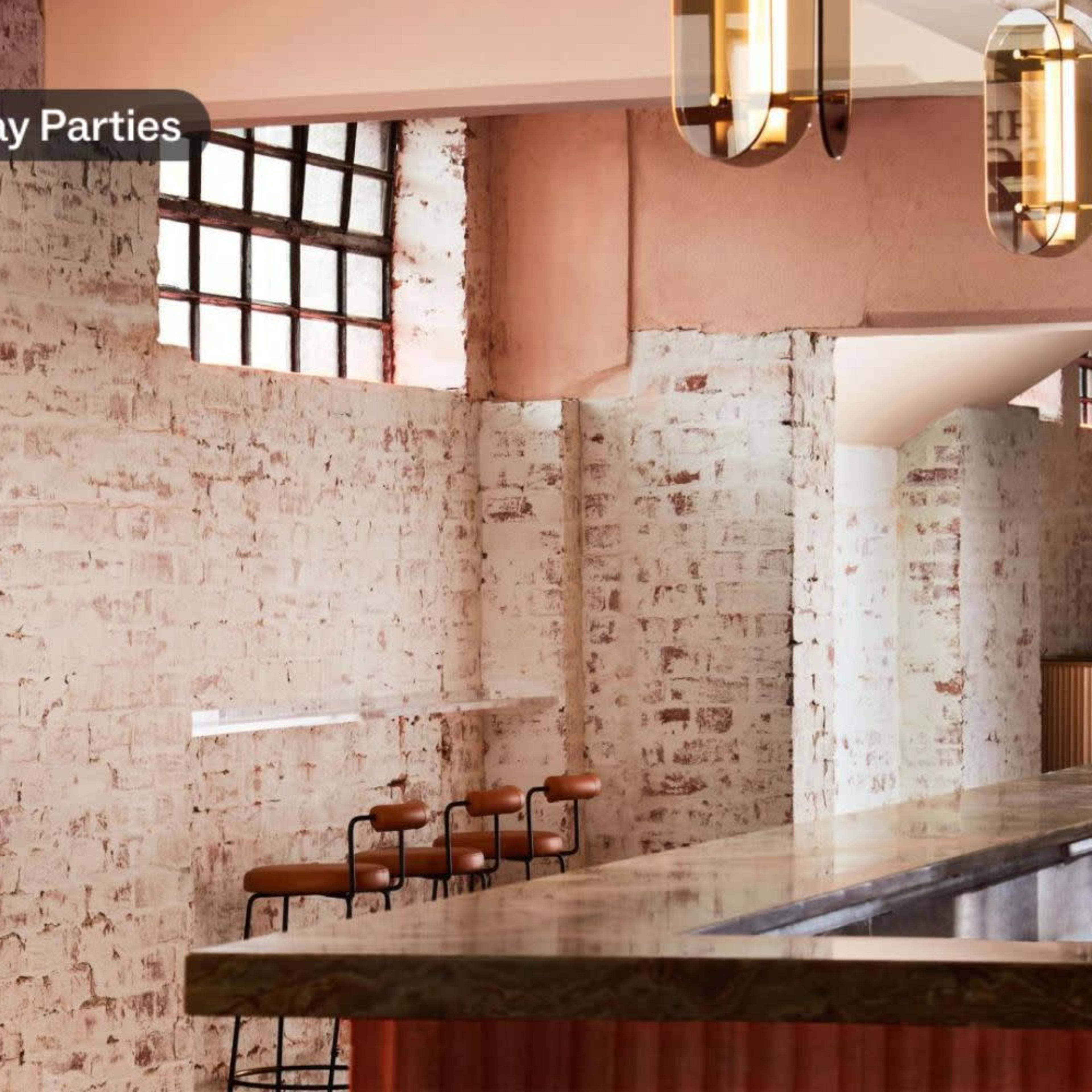 A well-lit interior with a bar, featuring a marble countertop, brass accents, and decorative elements including plants and flowers against a brick wall.