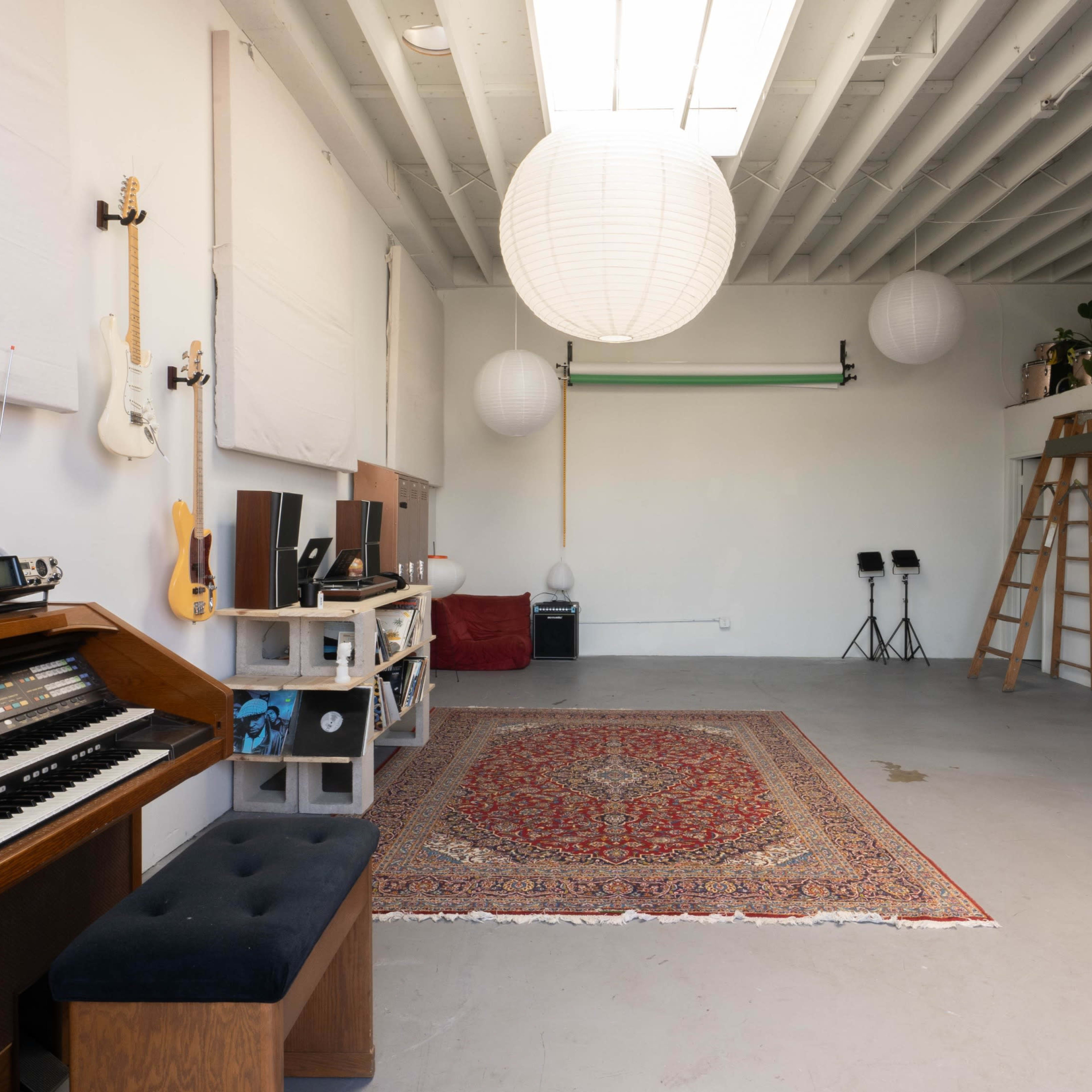 A spacious room features an organ, a large rug, and various musical instruments, with hanging lanterns and a ladder leading to a loft area.
