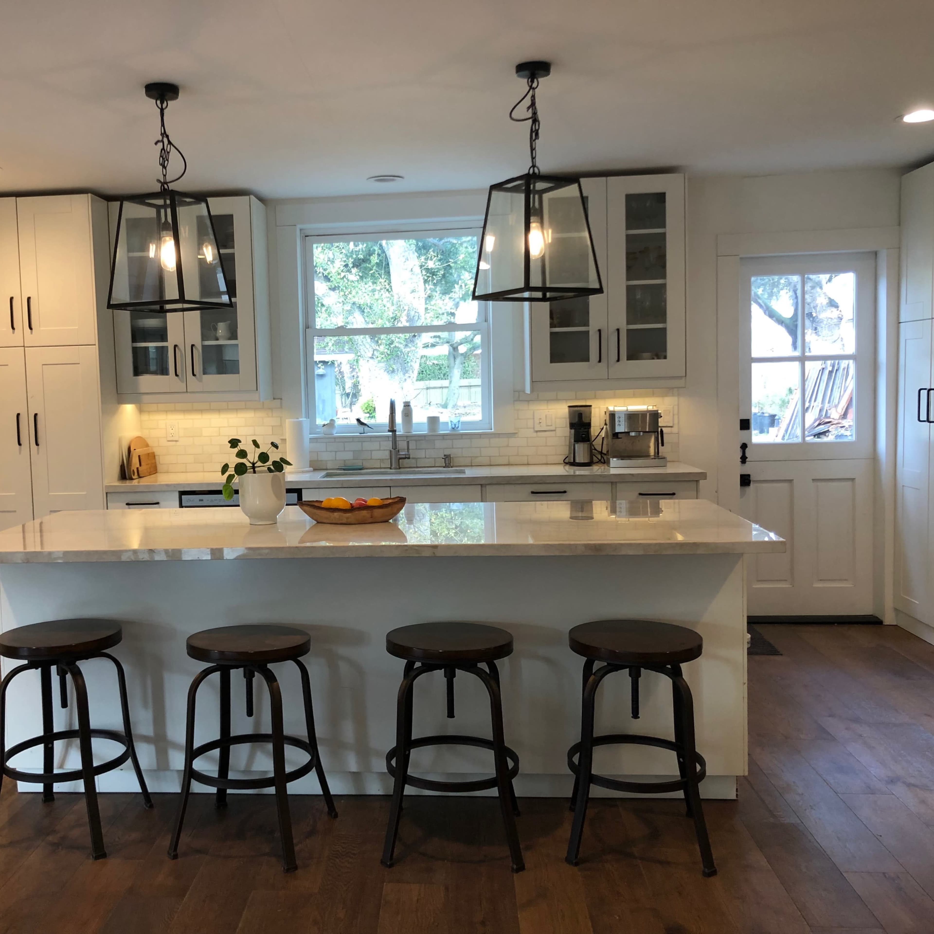 A modern kitchen features white cabinets, a large island with four wooden stools, and pendant lighting overhead.