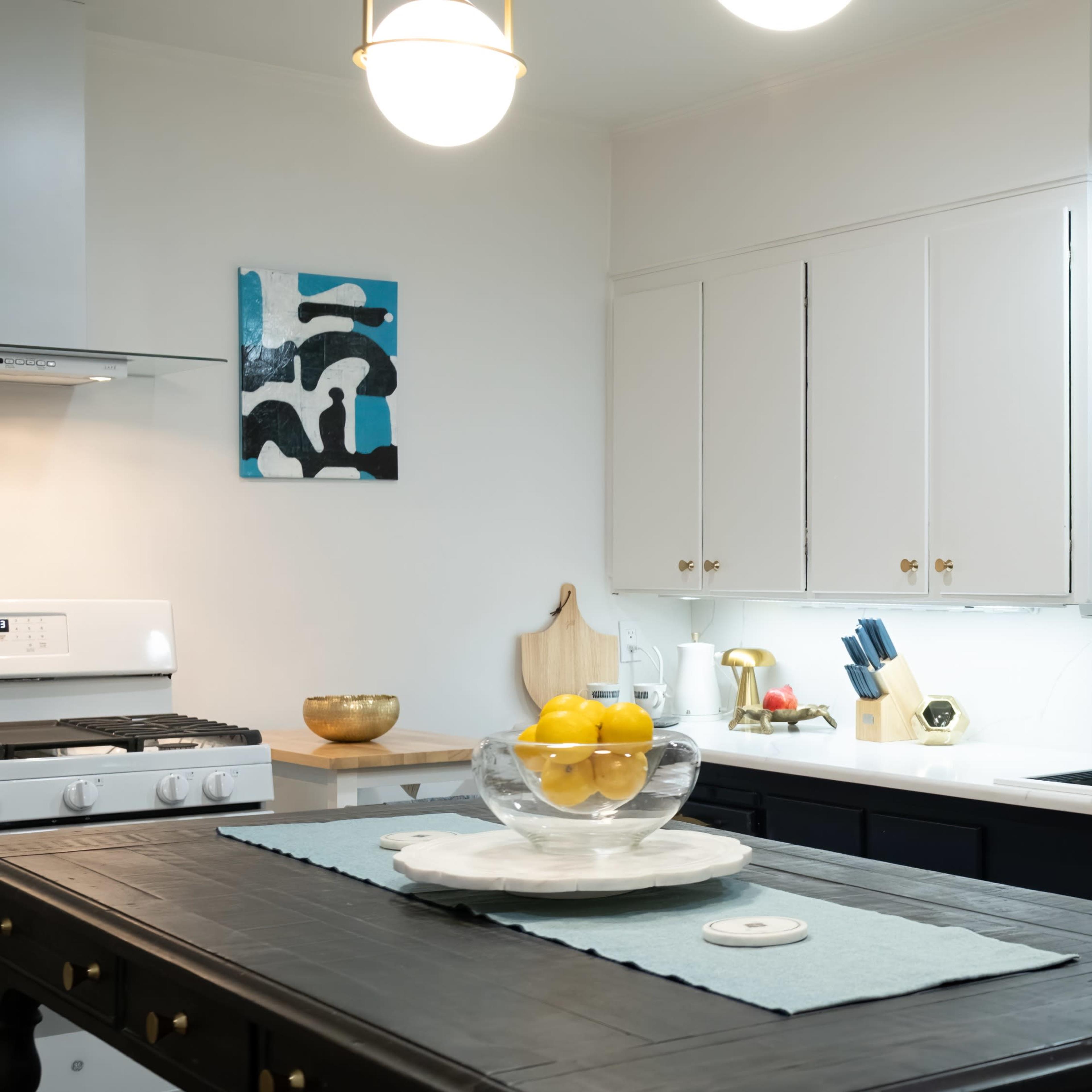 A modern kitchen featuring a central island with a bowl of lemons, white cabinetry, and stainless steel appliances.