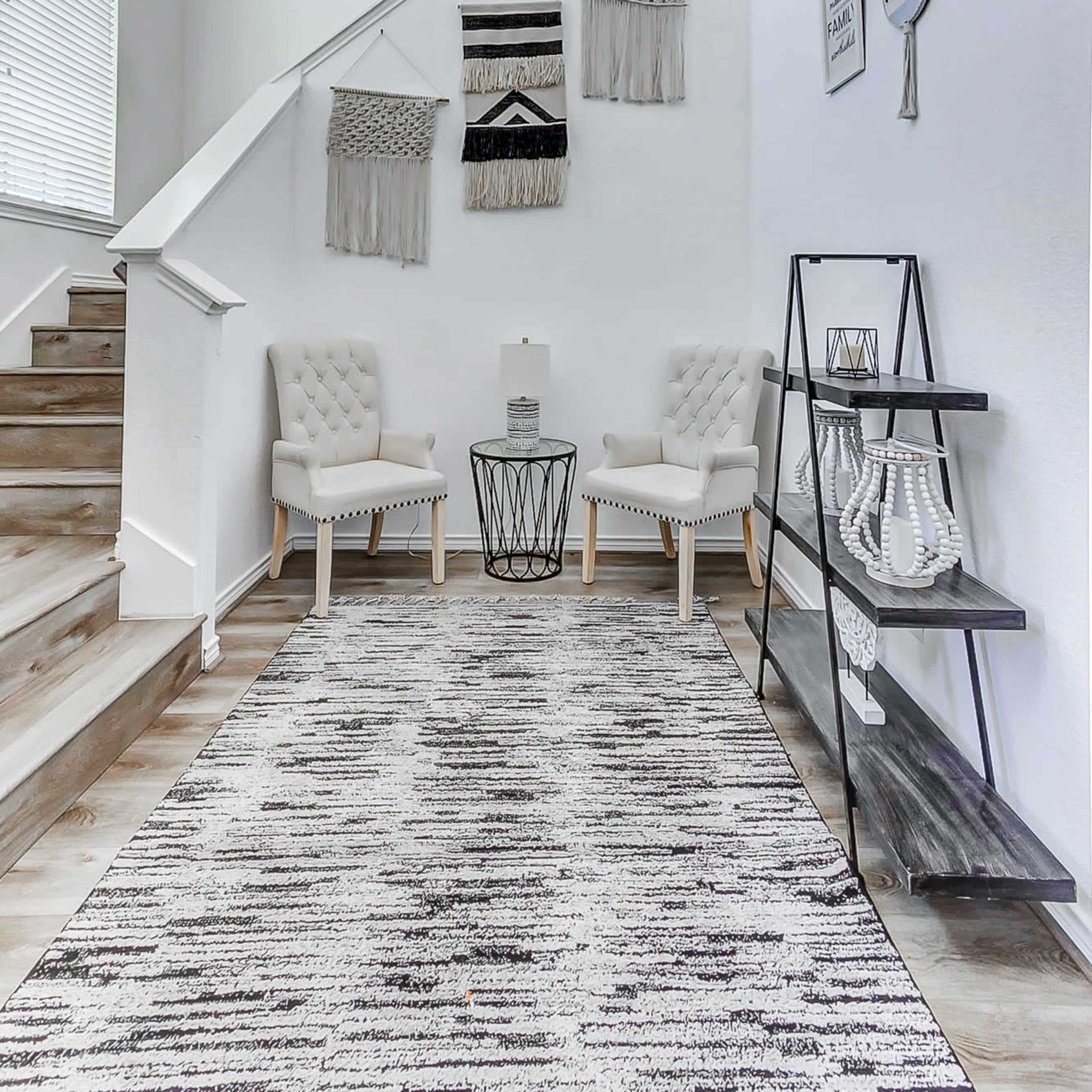 A modern entryway features two upholstered chairs, a circular table, and decorative wall hangings beside a staircase.