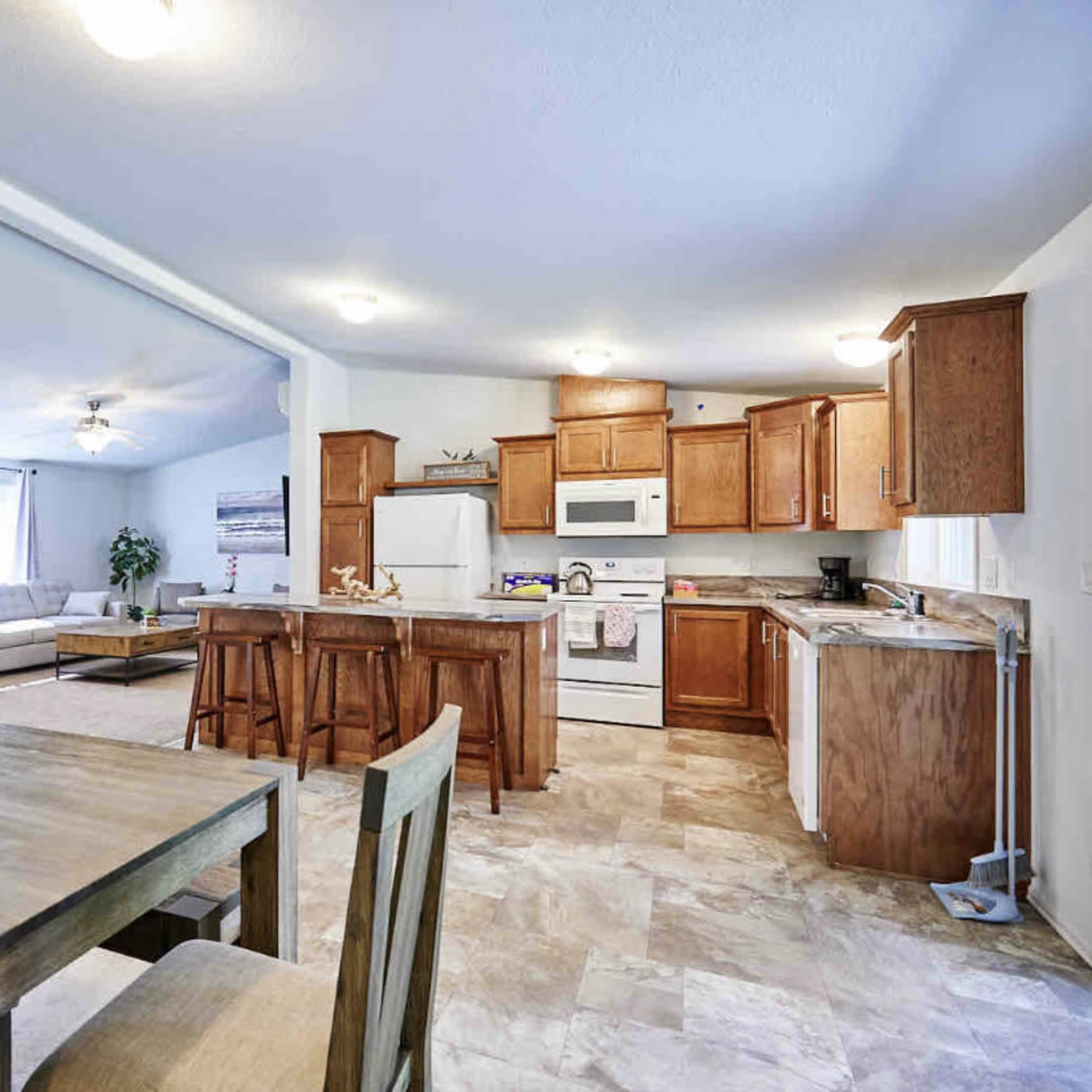 A bright, open kitchen and dining area with wooden cabinetry, a white refrigerator, and a dining table set for four.