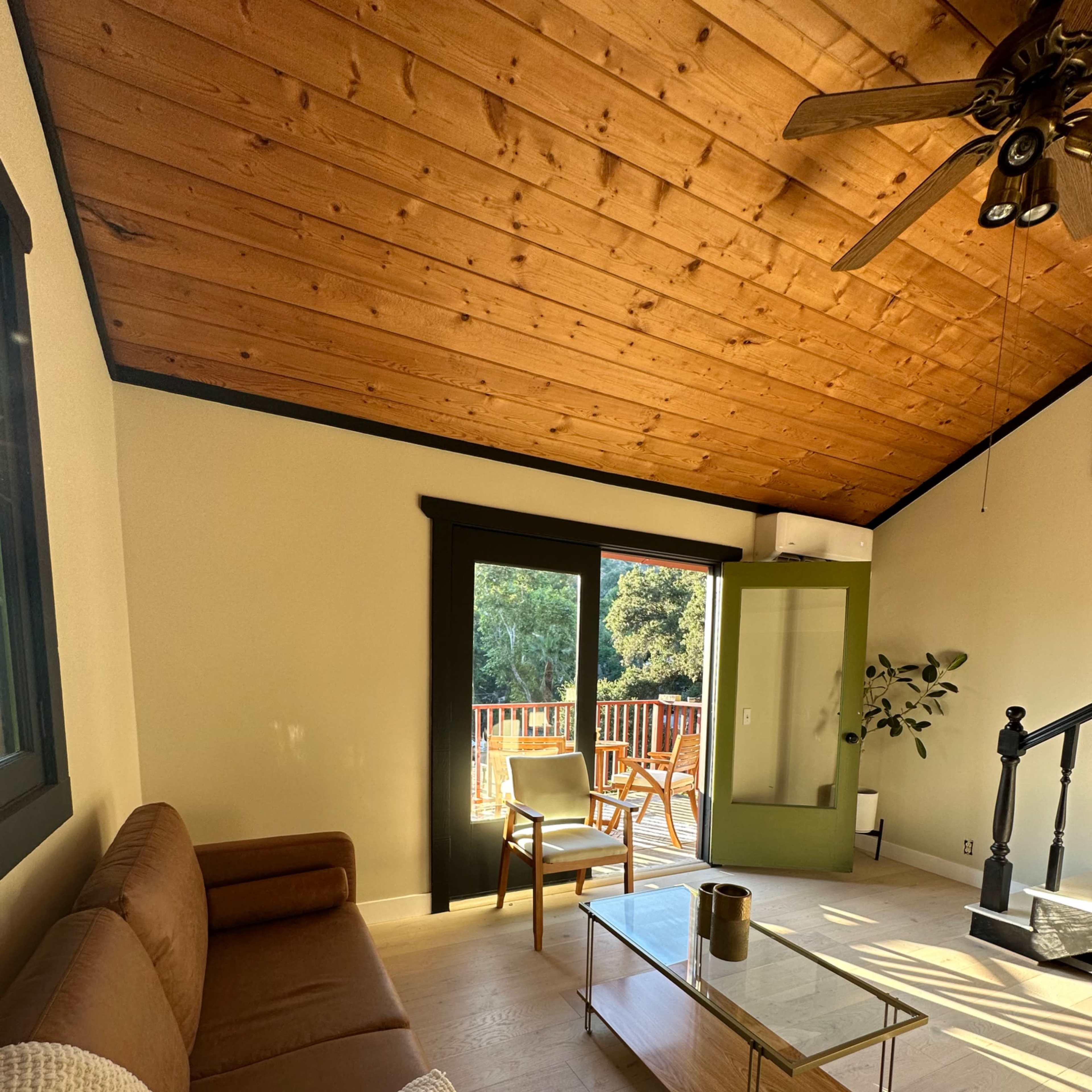 A well-lit living room with a brown sofa, a glass coffee table, and a door leading to an outdoor deck.