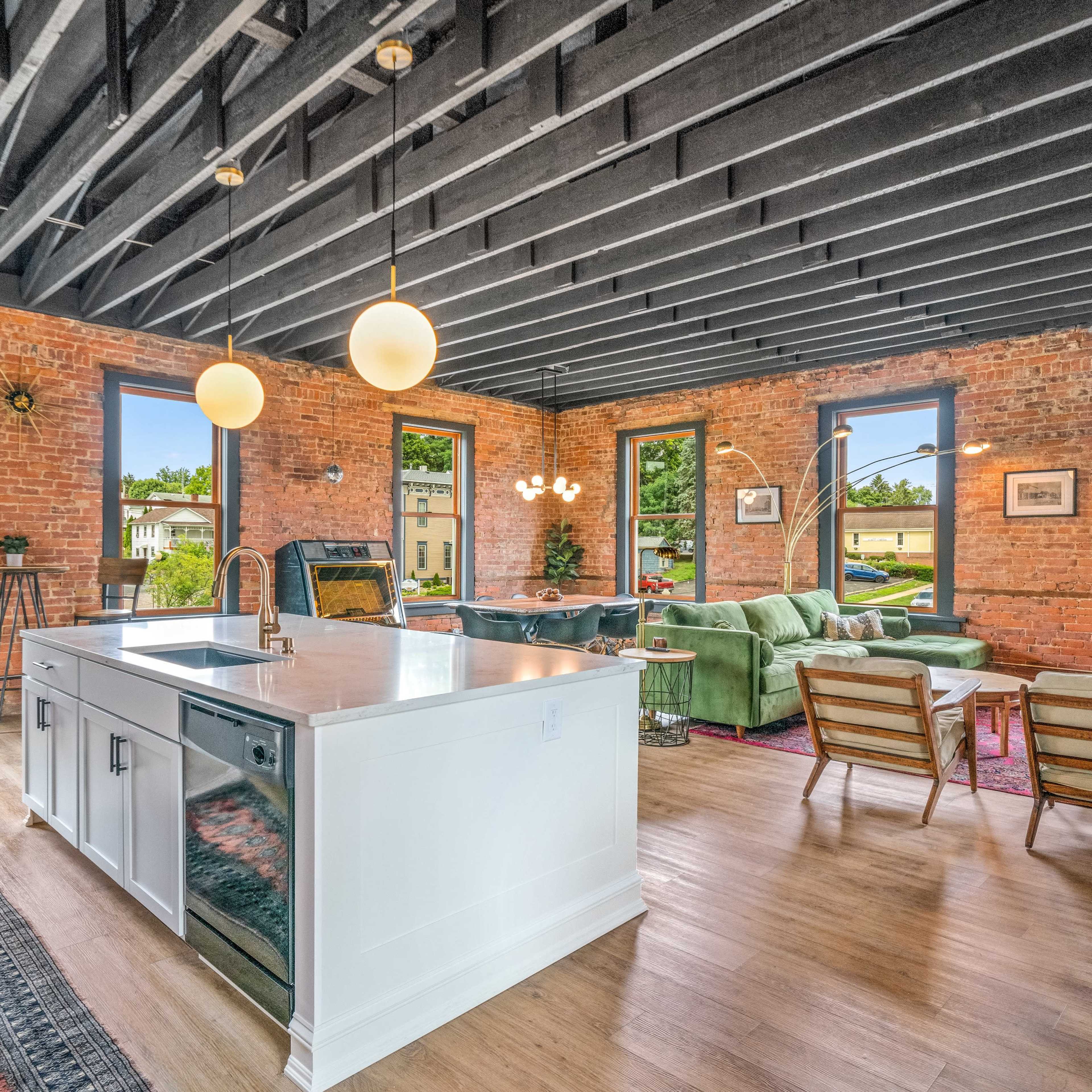 A spacious open-concept living area with a kitchen island, exposed brick walls, and large windows letting in natural light.