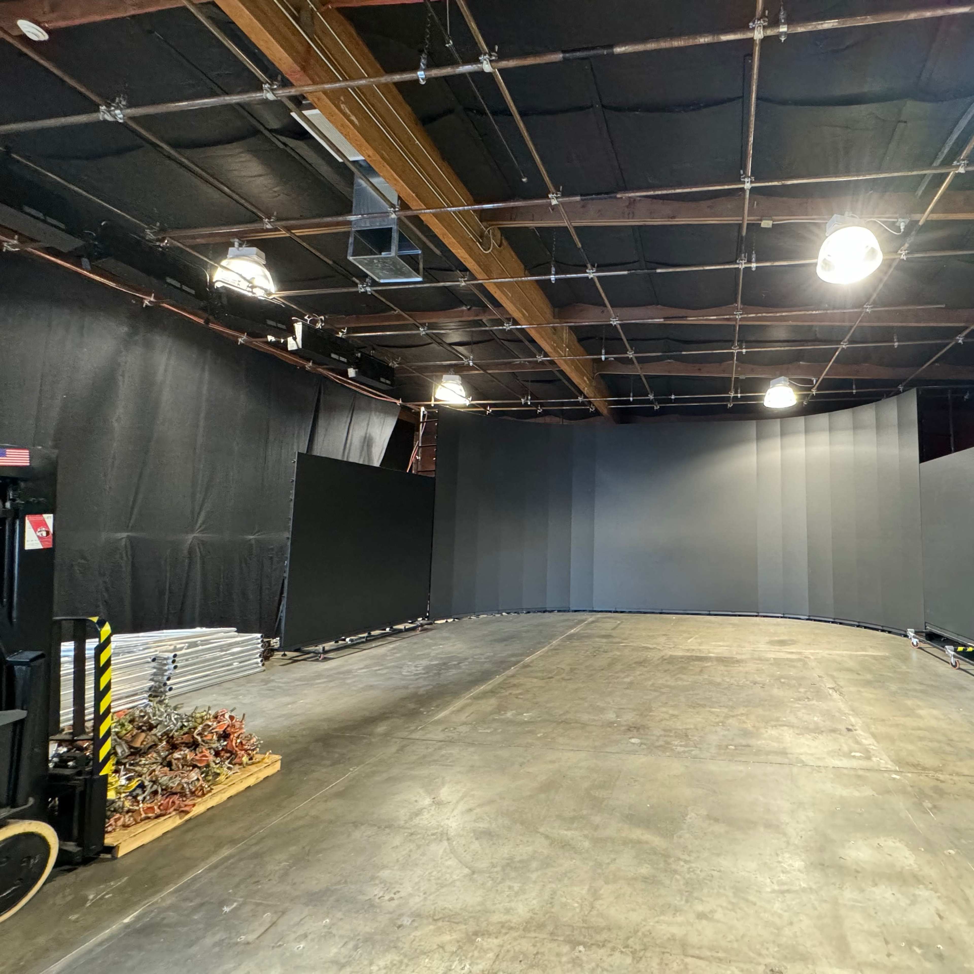 A large studio space with a curved backdrop, surrounded by black curtains and various equipment along the sides.