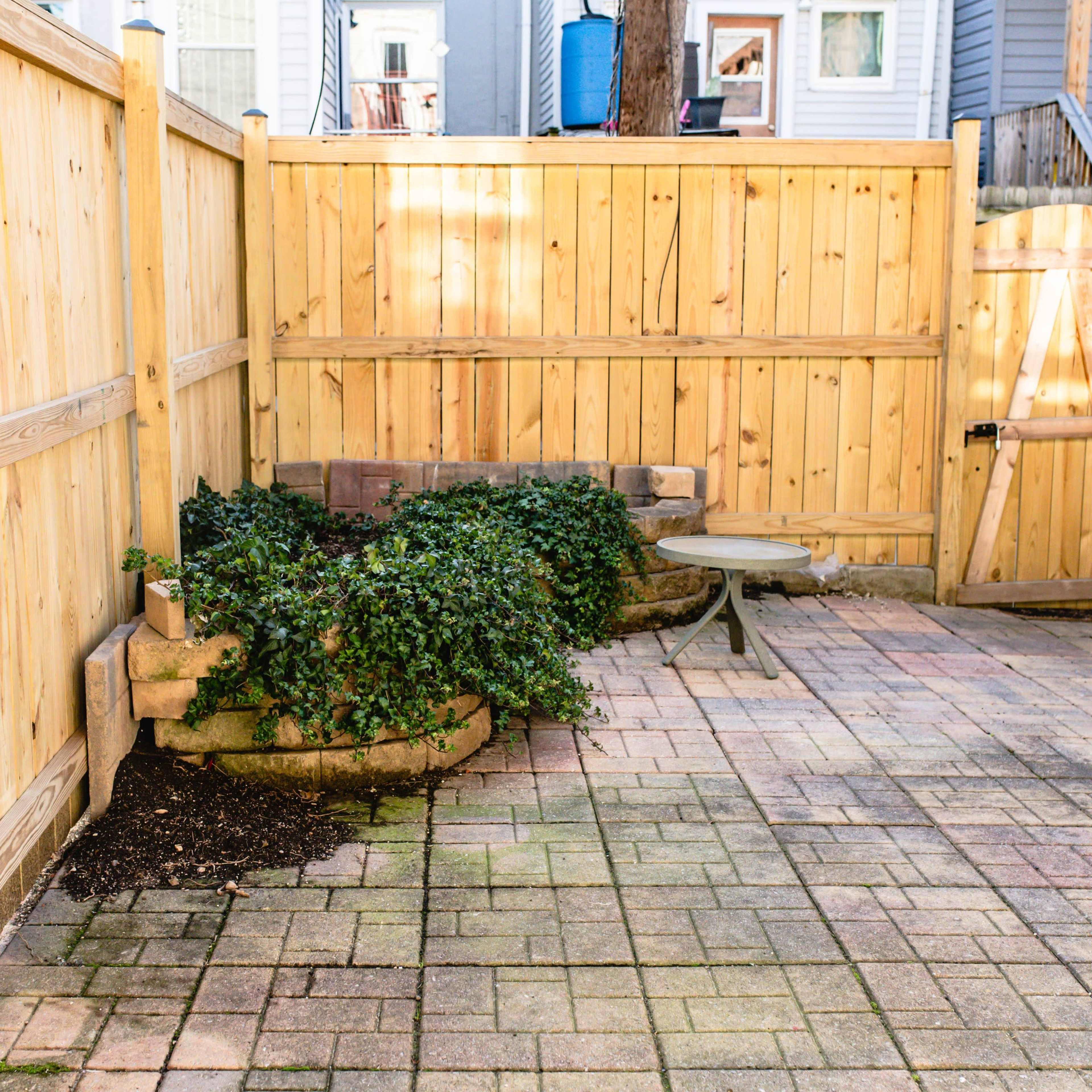 A small enclosed patio area with wooden fencing, a stone seating arrangement, and a patch of greenery.