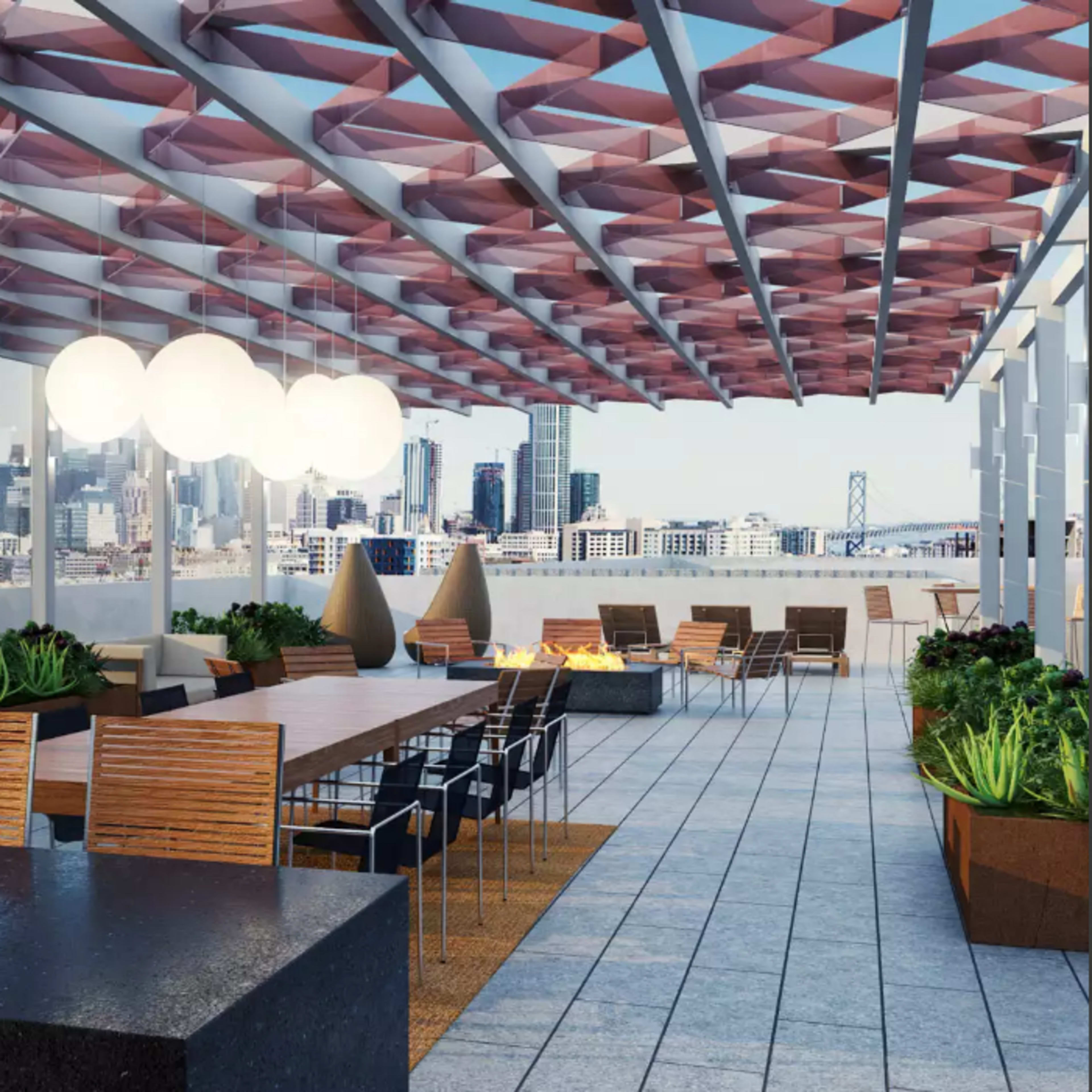 A rooftop terrace with a long table, outdoor seating, and city skyline views in the background.