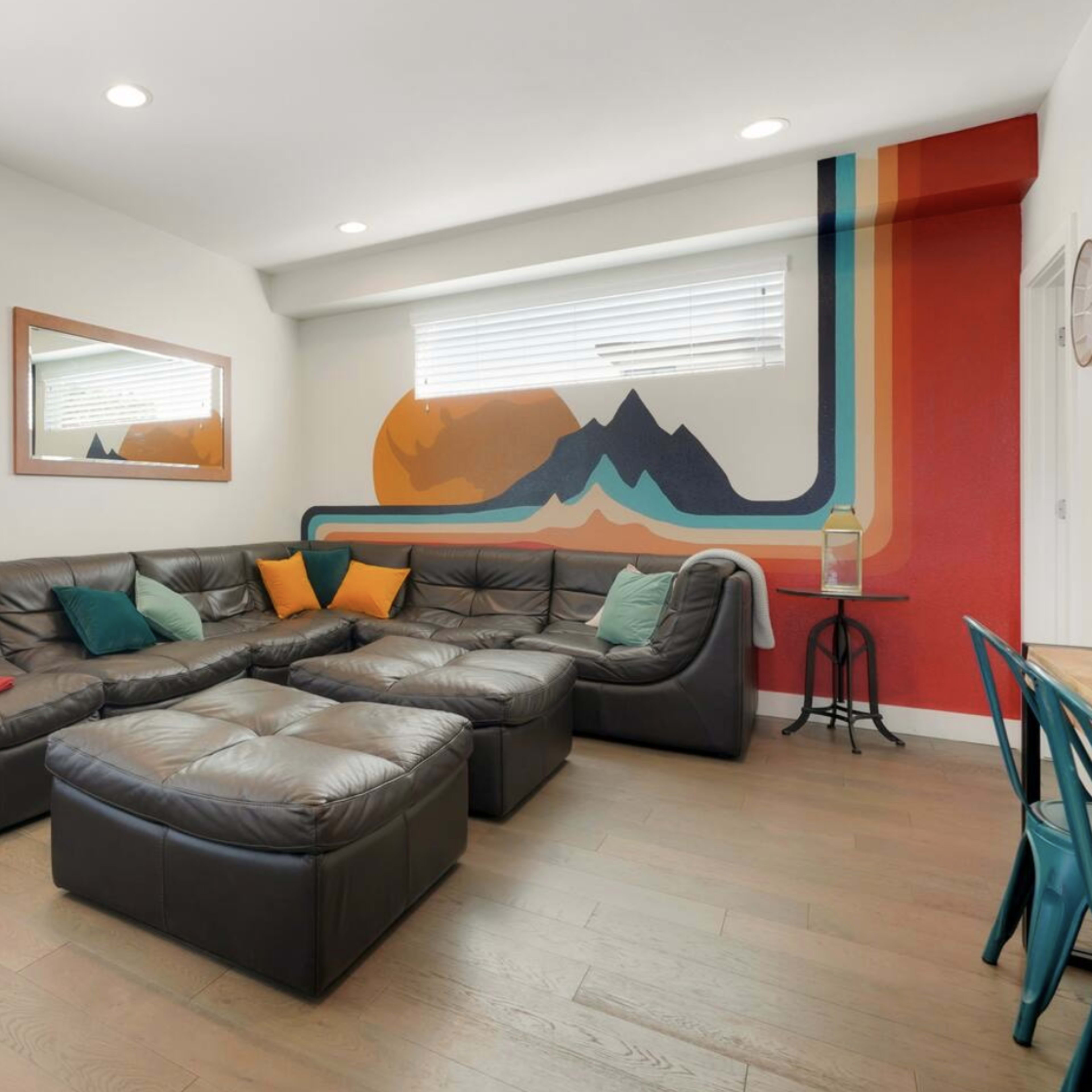 The living room features a large sectional couch, a hammock, a decorative mountain mural on the wall, and wooden flooring.