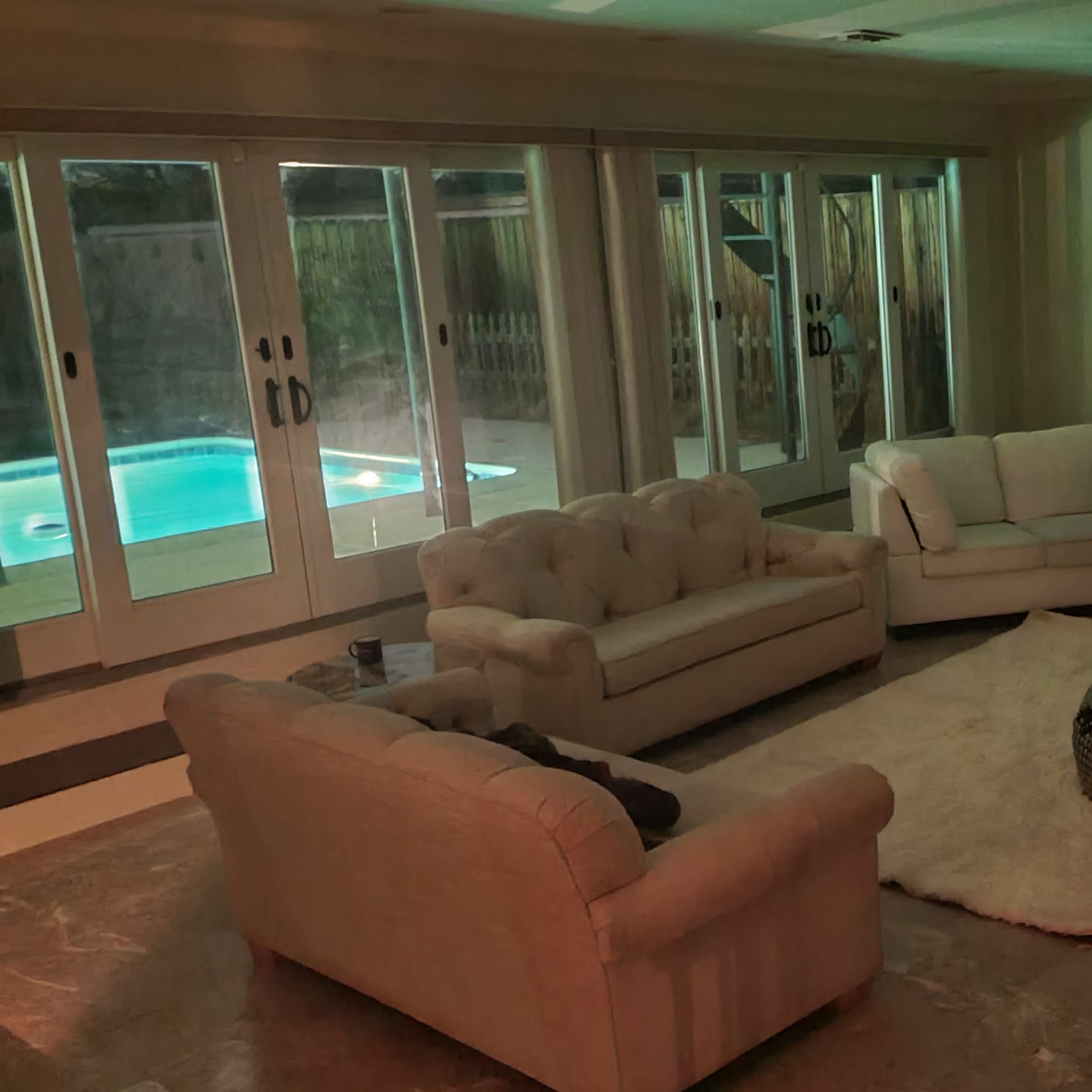 A spacious living room with light-colored furniture, including a sectional sofa and two armchairs, arranged around a round coffee table on a large area rug.