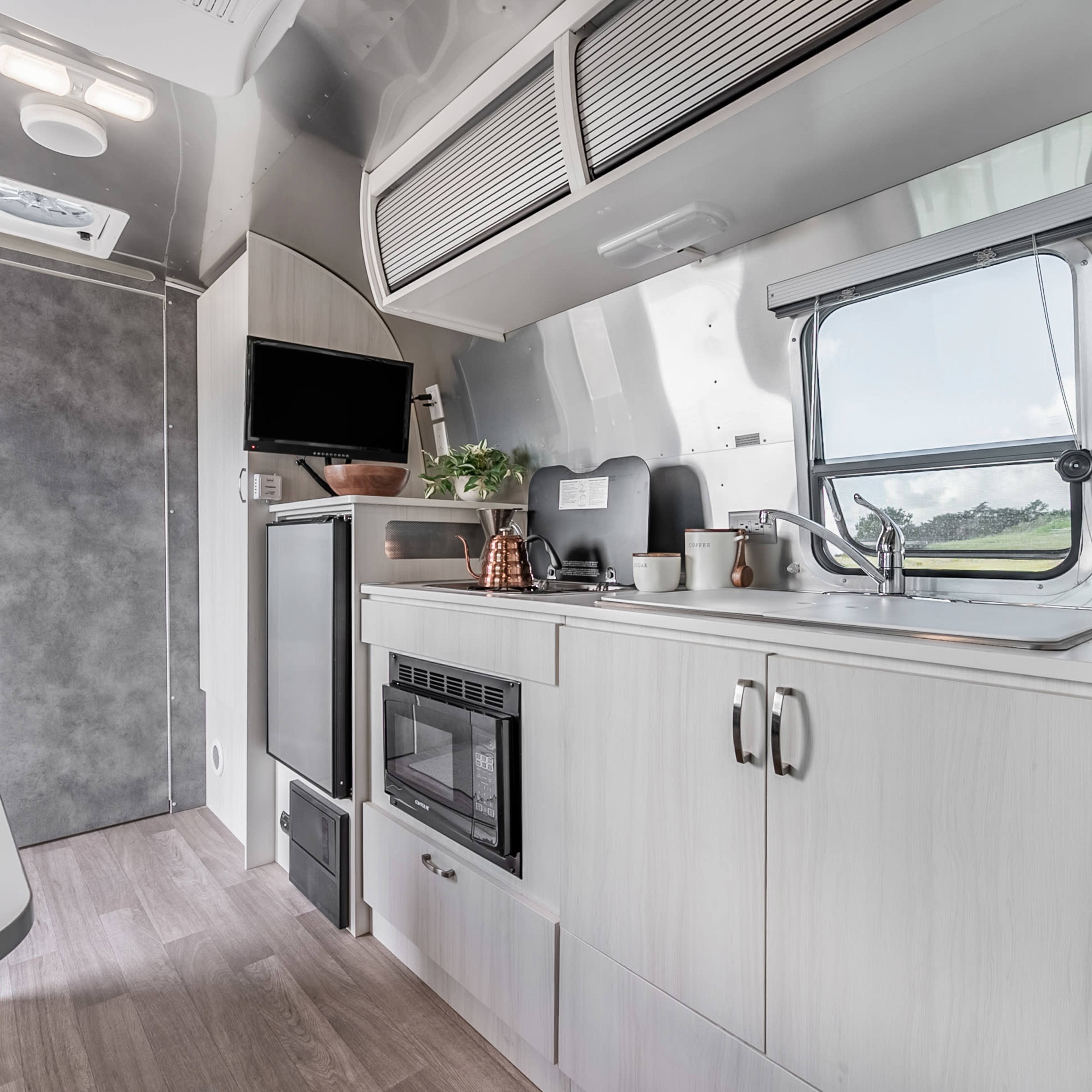 The interior of a modern camper trailer with kitchen amenities, including a sink, refrigerator, and a small dining area.