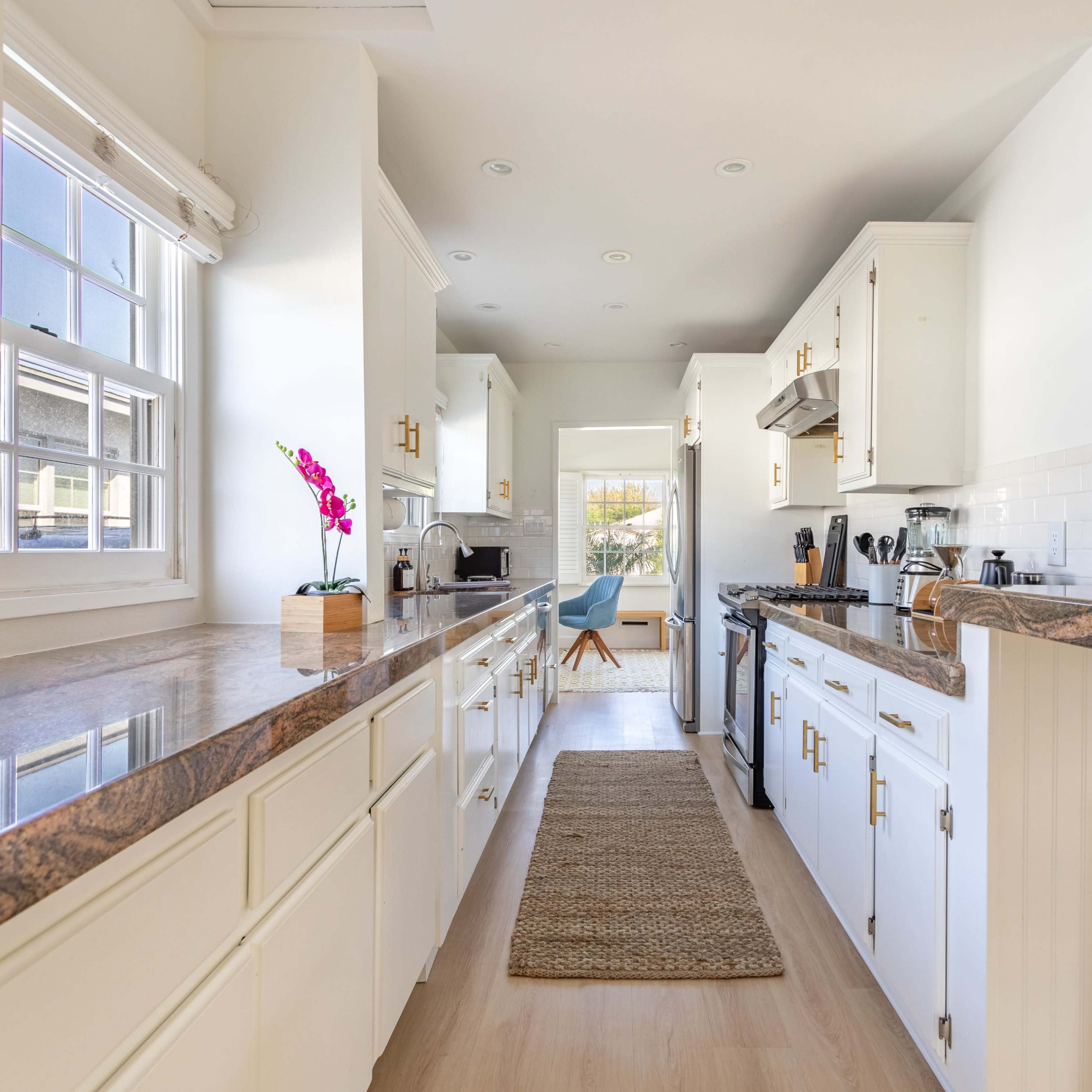 A modern kitchen with white cabinets, a dark granite countertop, and a small dining area at the end.