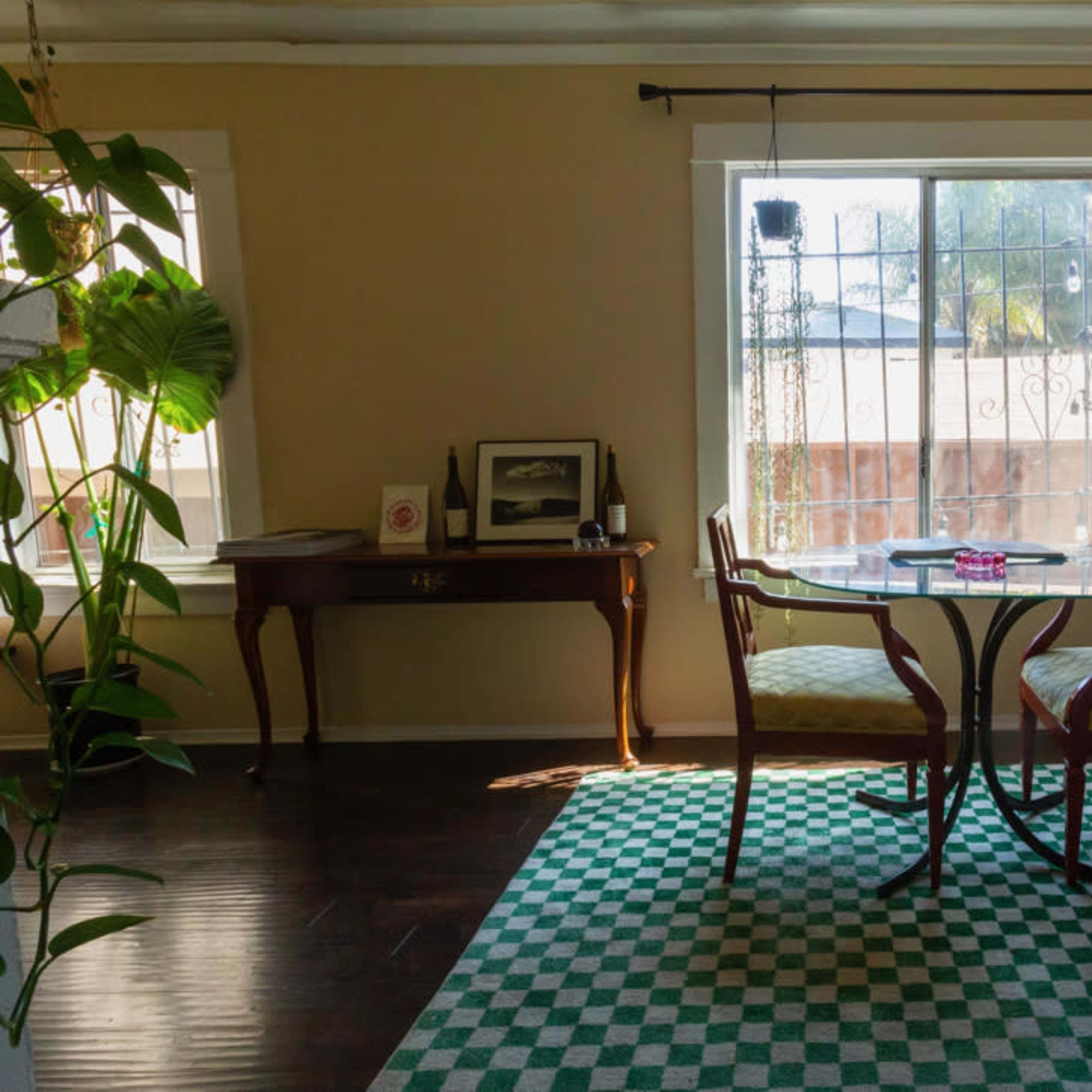A small dining area features a round table set for two, with a patterned rug on the floor and a window that allows natural light to enter.