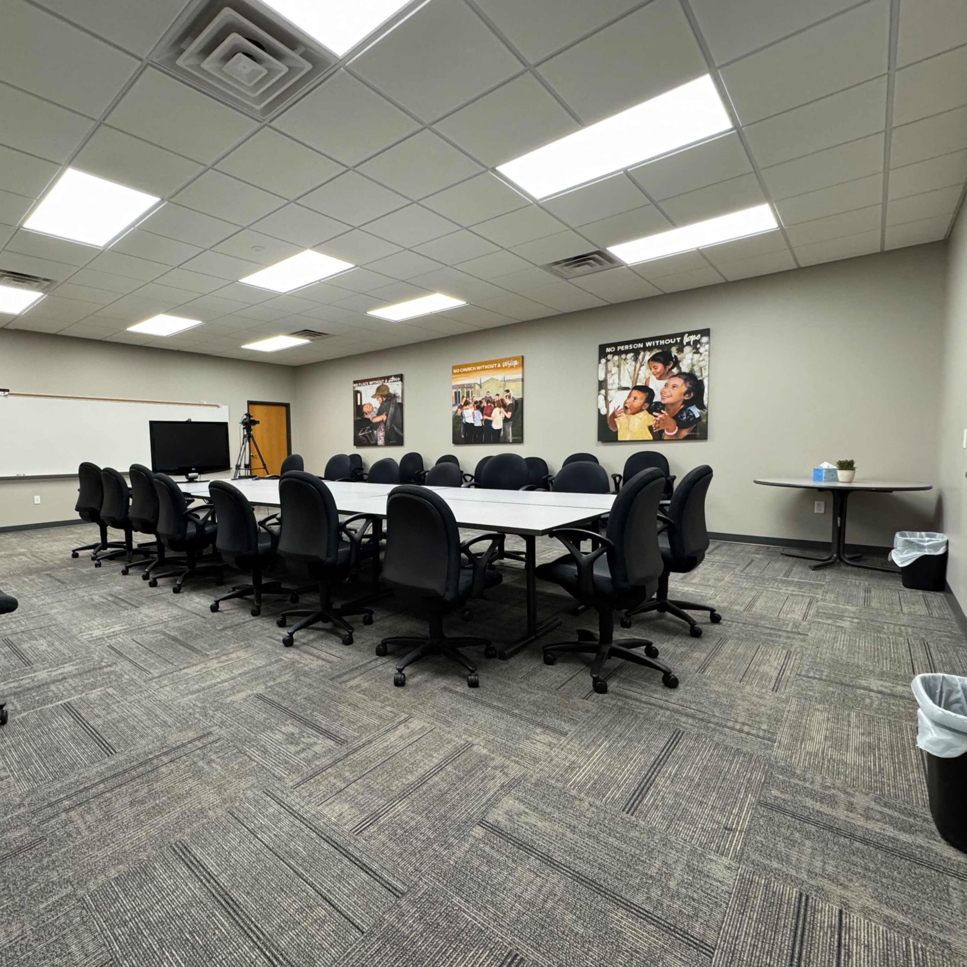 A spacious conference room with a large rectangular table surrounded by black office chairs, and photographs on the walls.