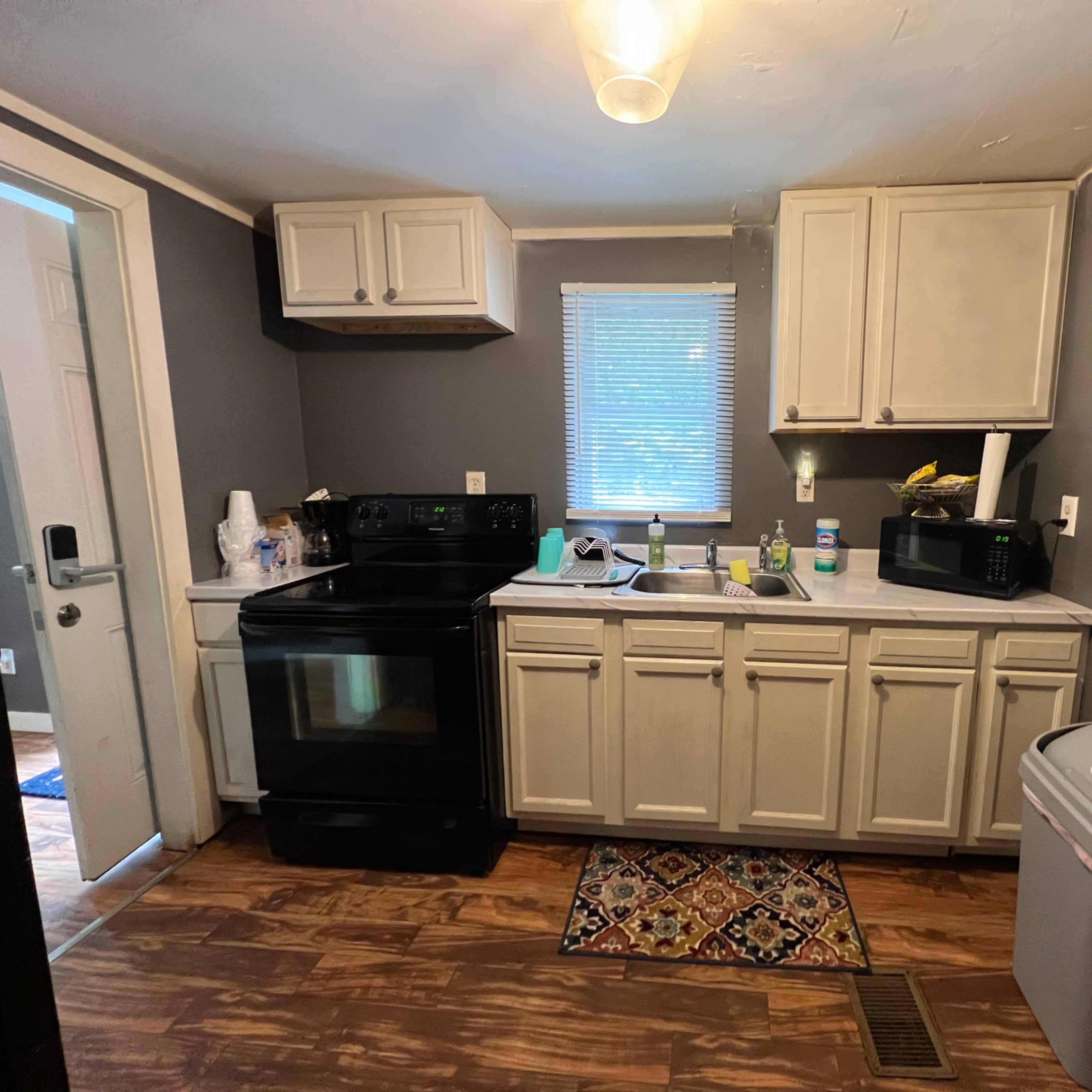 A small kitchen with white cabinets, a black stove, and a sink area with various kitchen items and appliances.