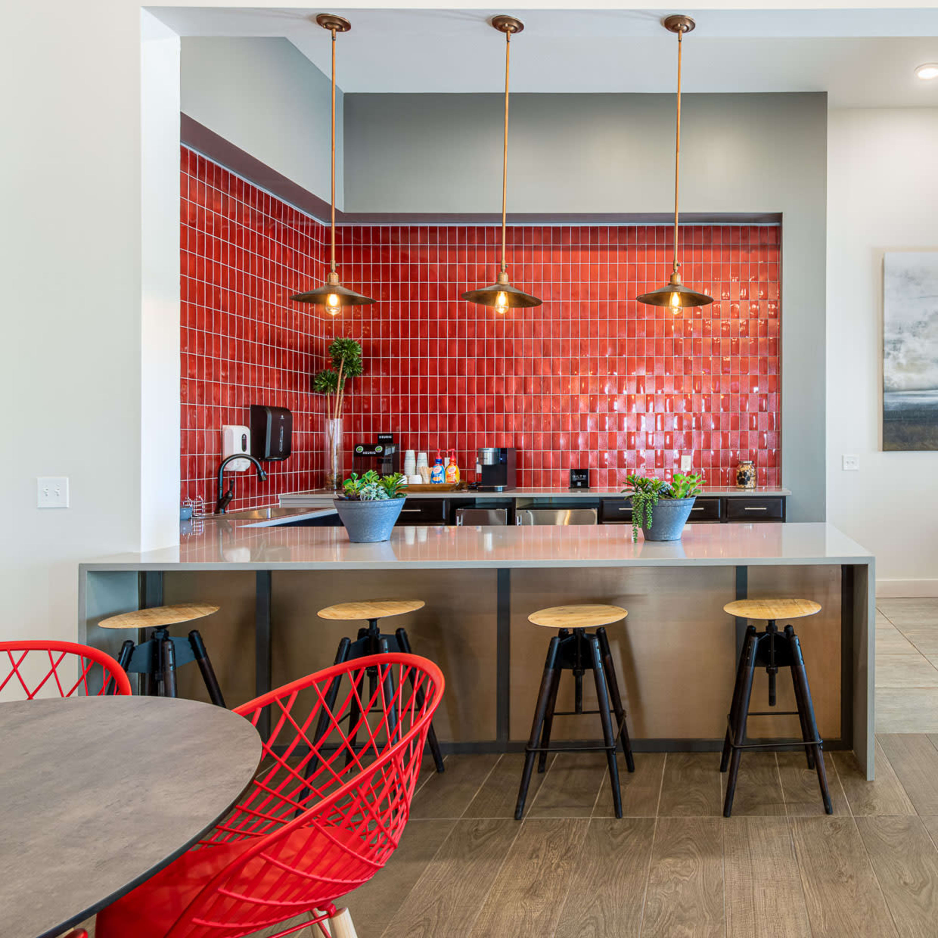 A modern kitchen featuring a red tiled backsplash, a central island with bar stools, and several dining tables.