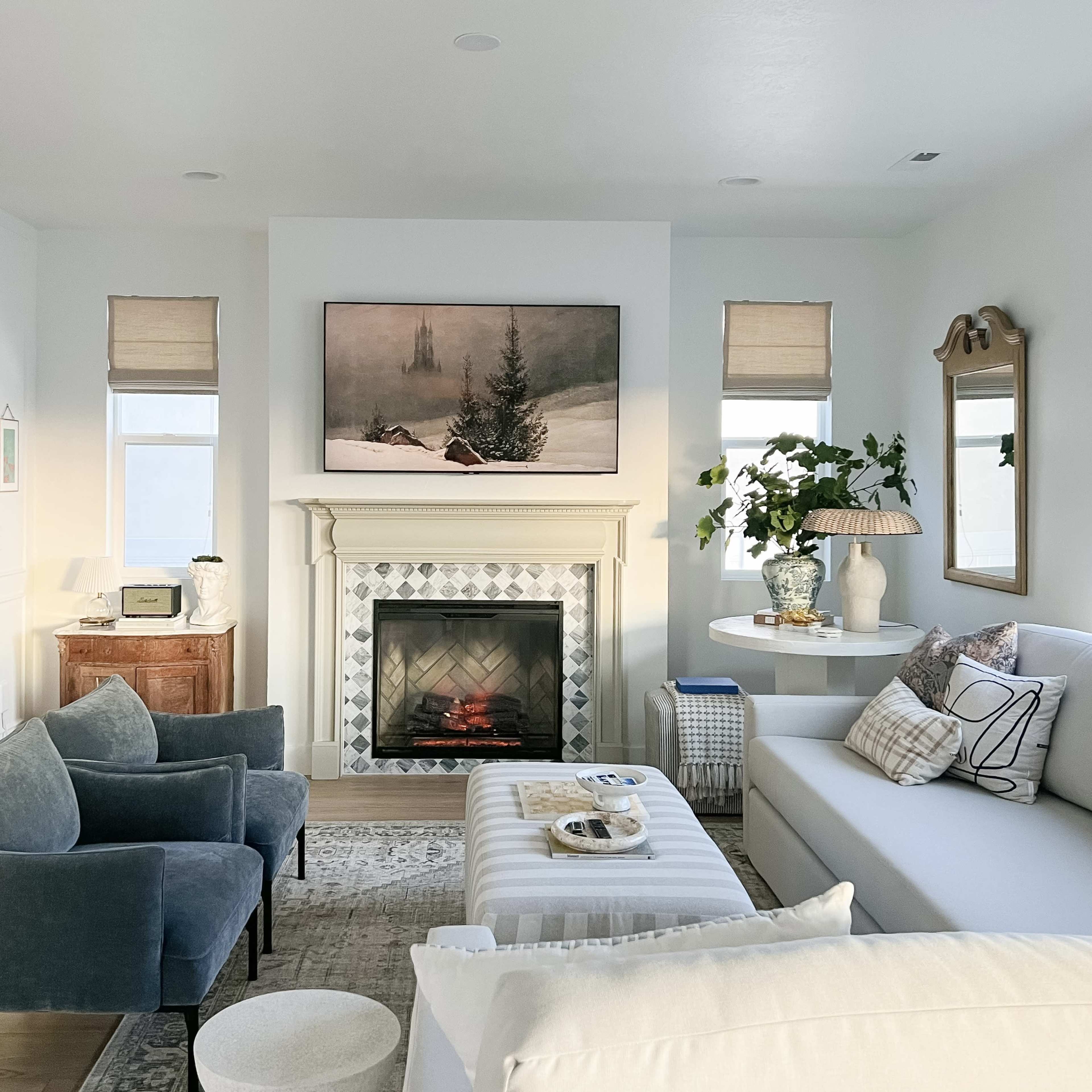 A modern living room featuring a fireplace, a large wall-mounted television displaying a winter scene, and a combination of light-colored furniture and decor.
