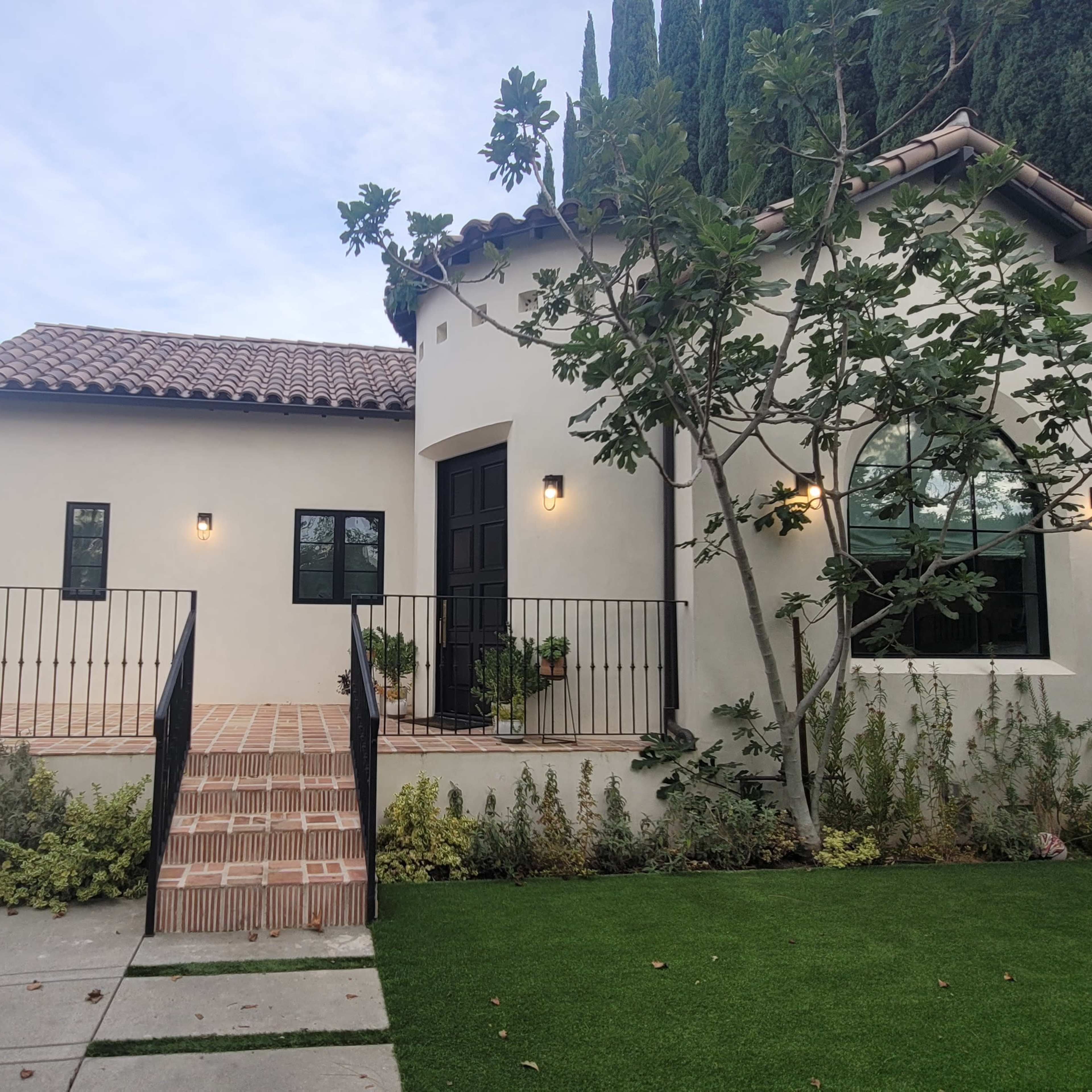 A modern house with a tiled roof, a front patio, and a landscaped yard featuring shrubs and greenery.