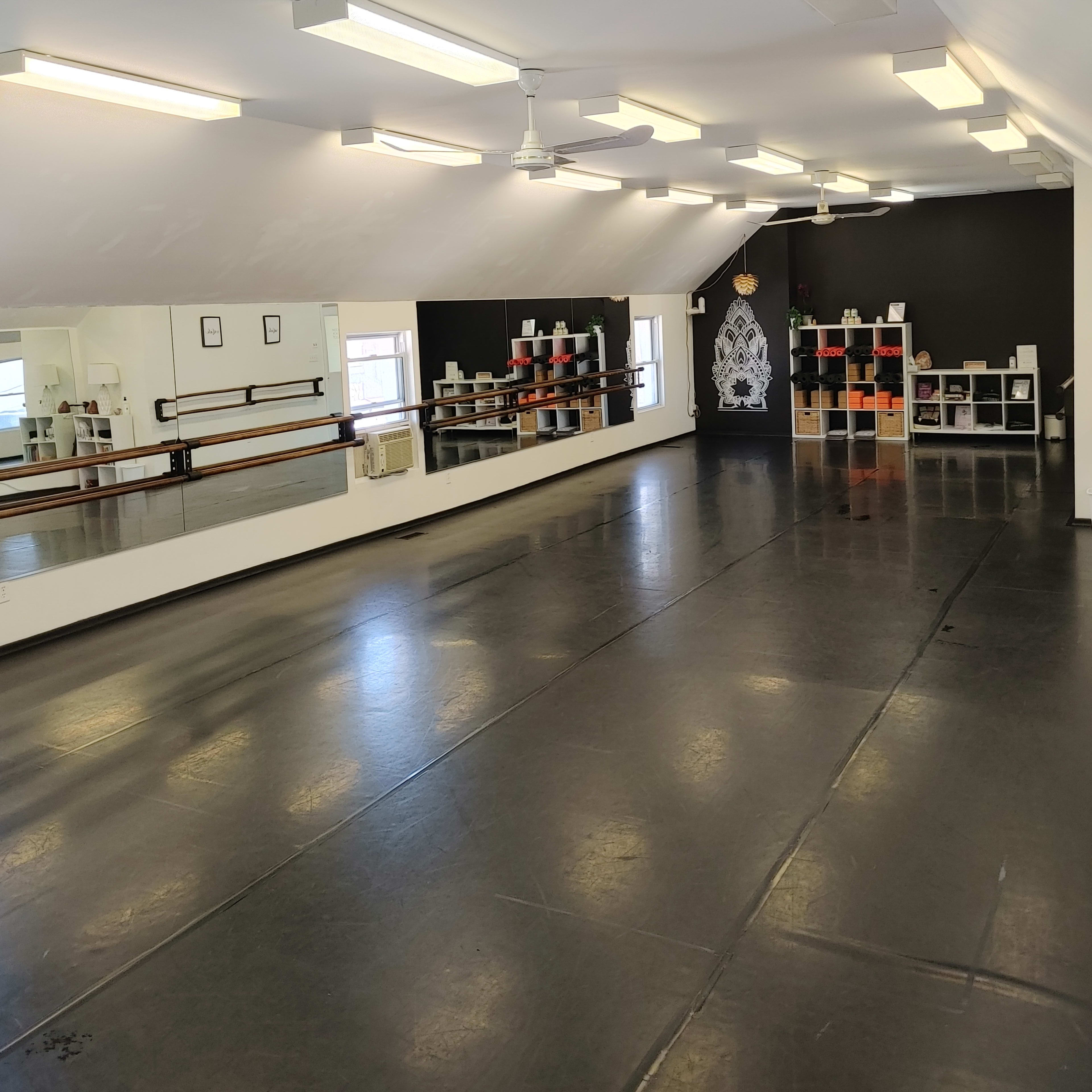 An empty dance studio with mirrored walls, black flooring, and shelves of colorful blocks along one side.