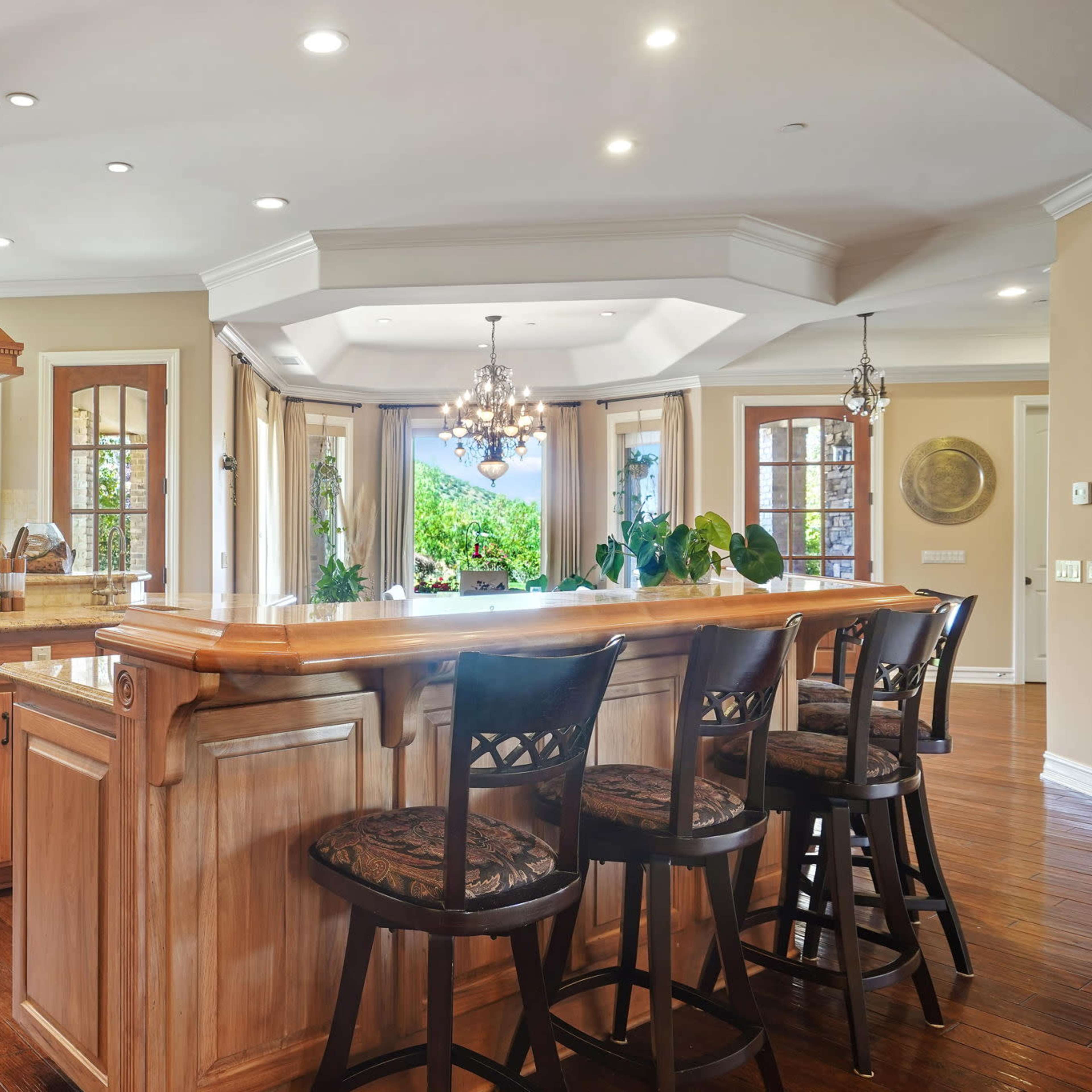 The kitchen features wooden cabinetry, a central island with seating, and large windows that allow natural light to illuminate the space.