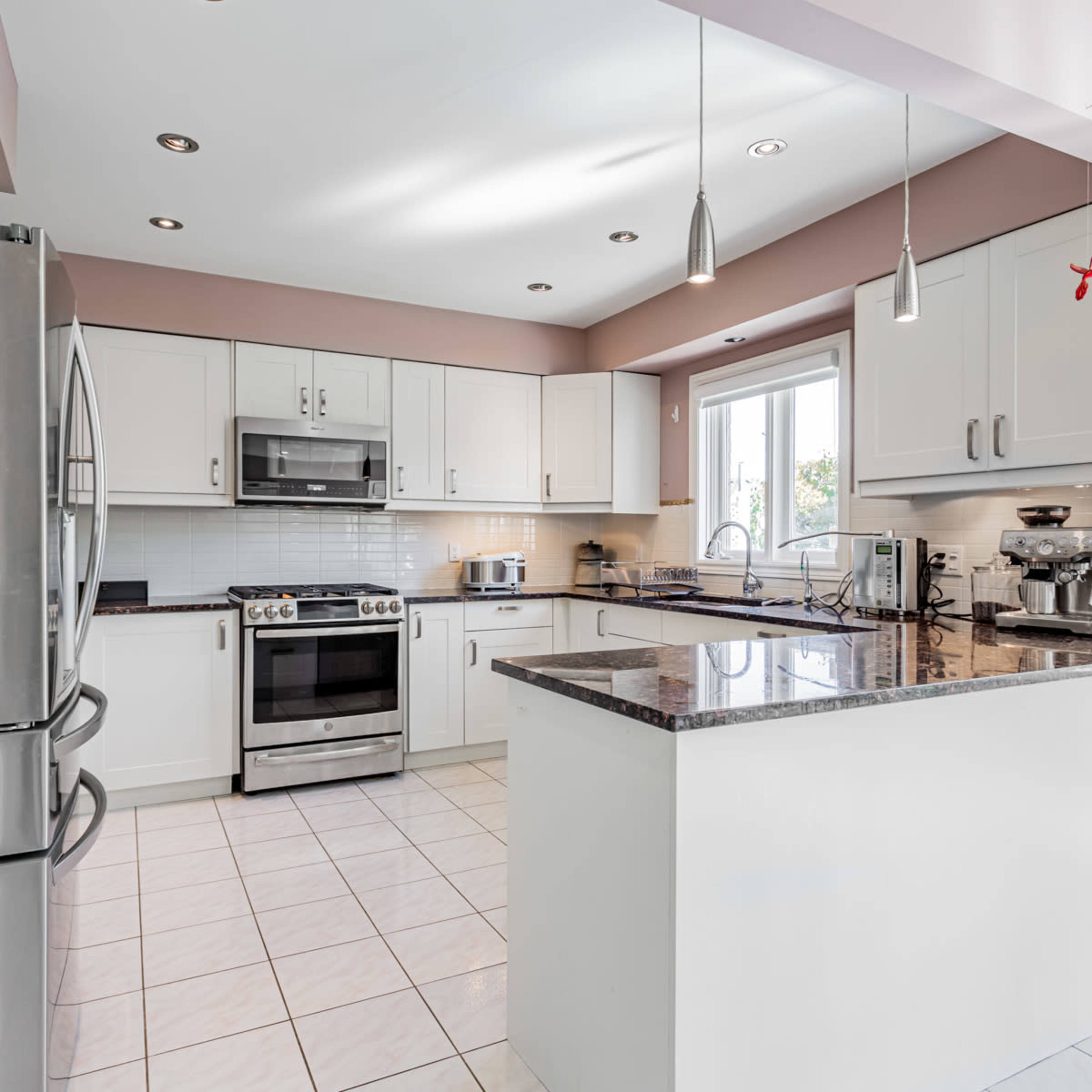 A modern kitchen features stainless steel appliances, white cabinets, and a granite countertop with tile flooring.