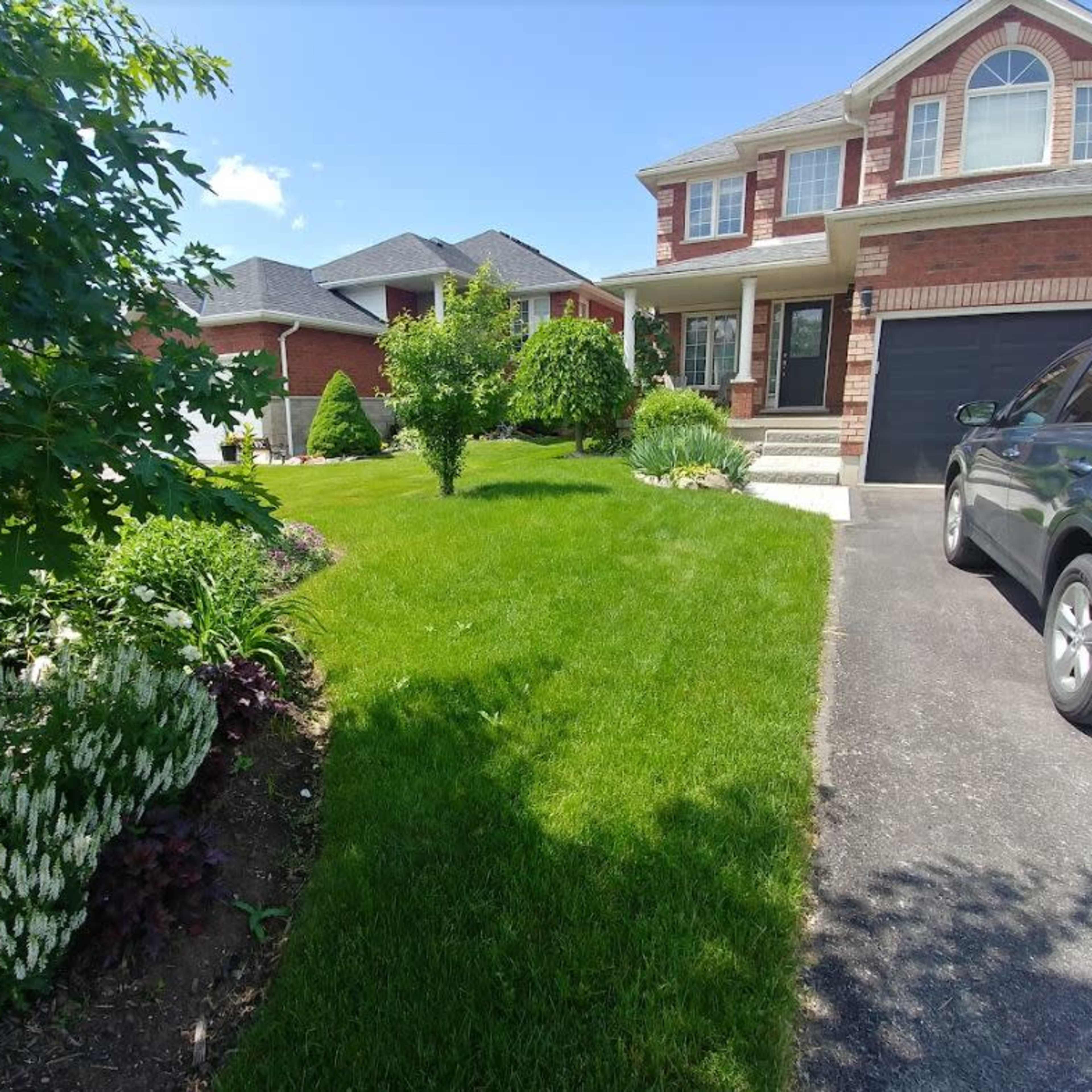 A well-maintained front yard of a brick house with landscaped gardens and a parked vehicle on the driveway.