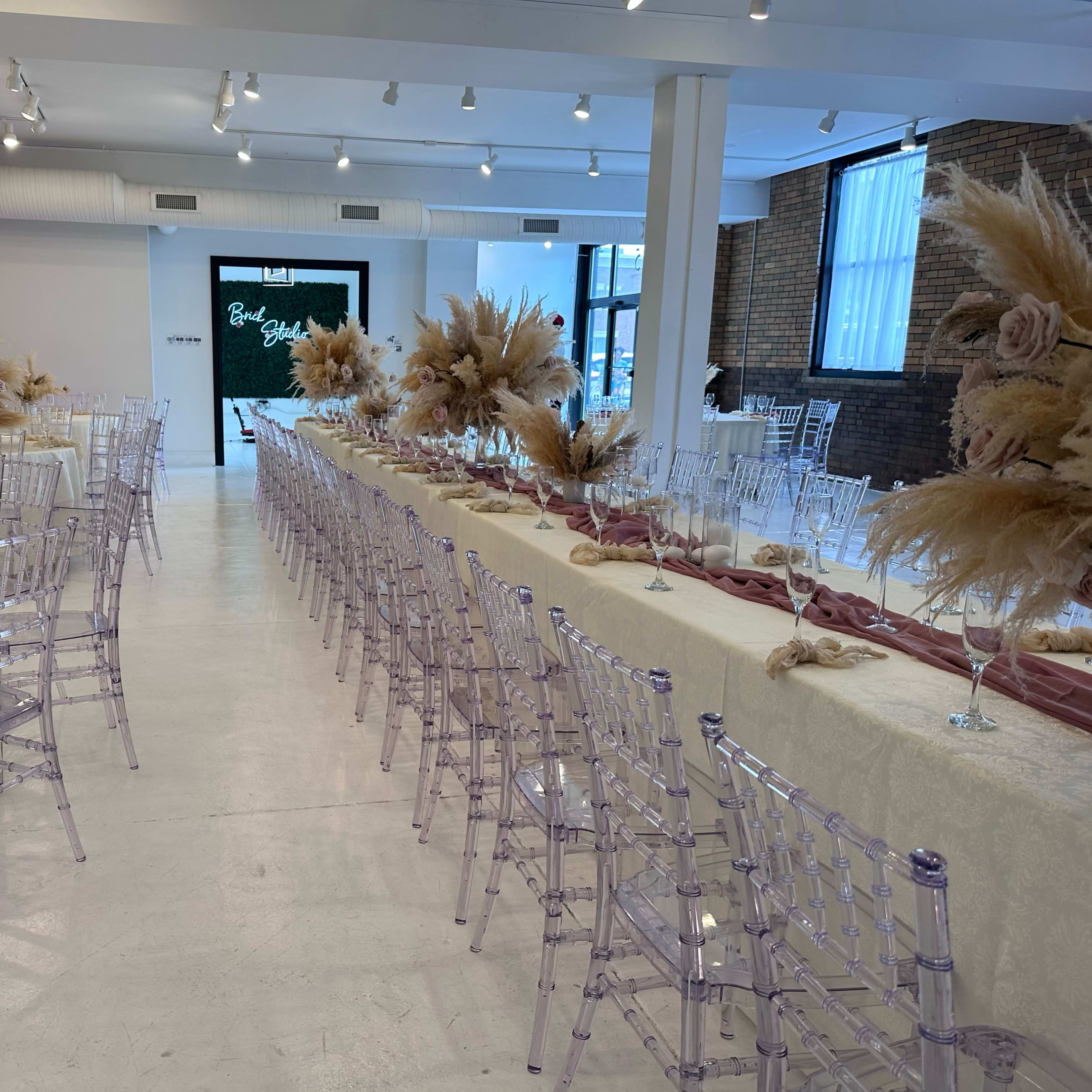 A spacious event hall features long tables set with elegant decor and floral arrangements, illuminated by bright overhead lights.