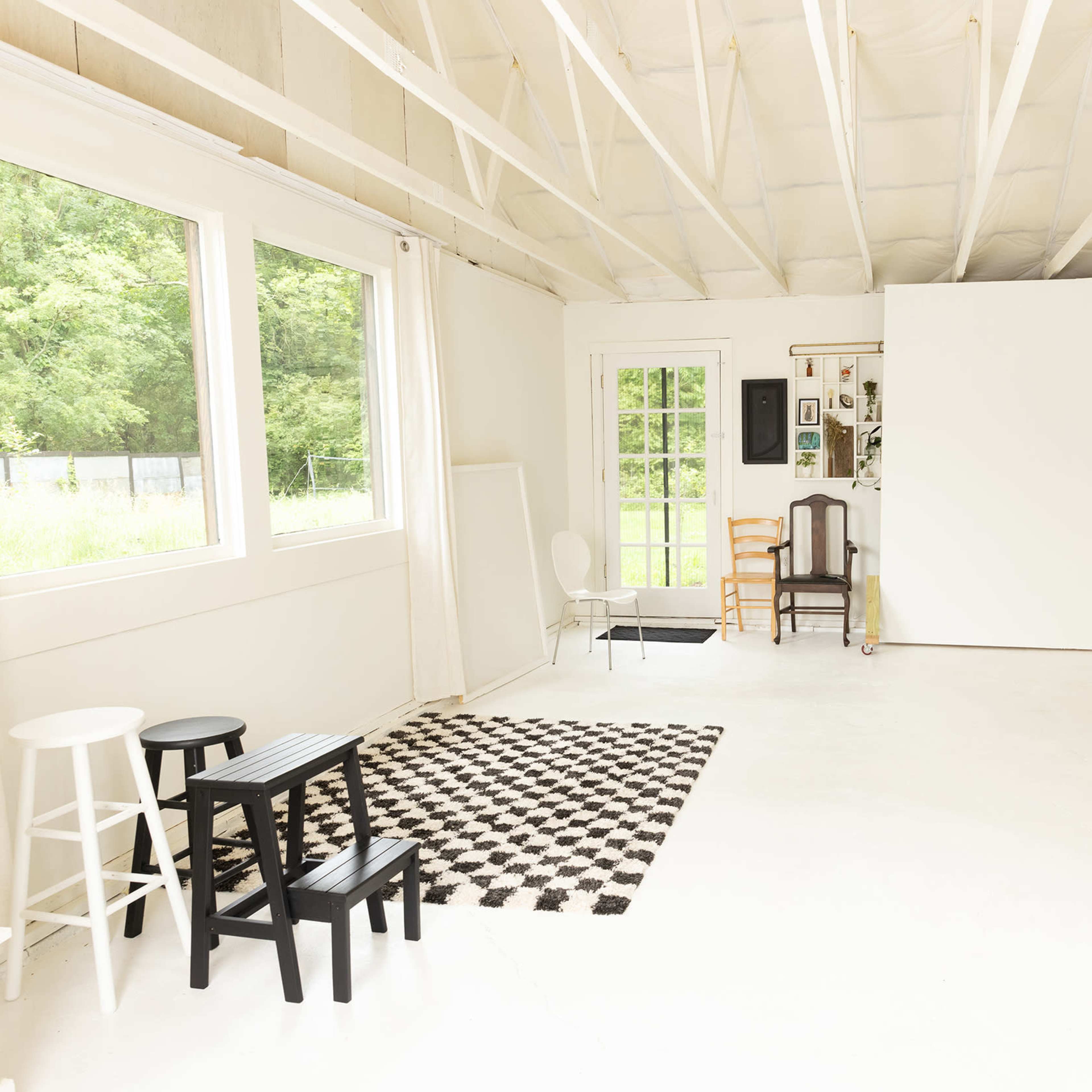 A bright, spacious room with white walls, large windows, and a large blank screen at one end, furnished with various chairs and a patterned rug.