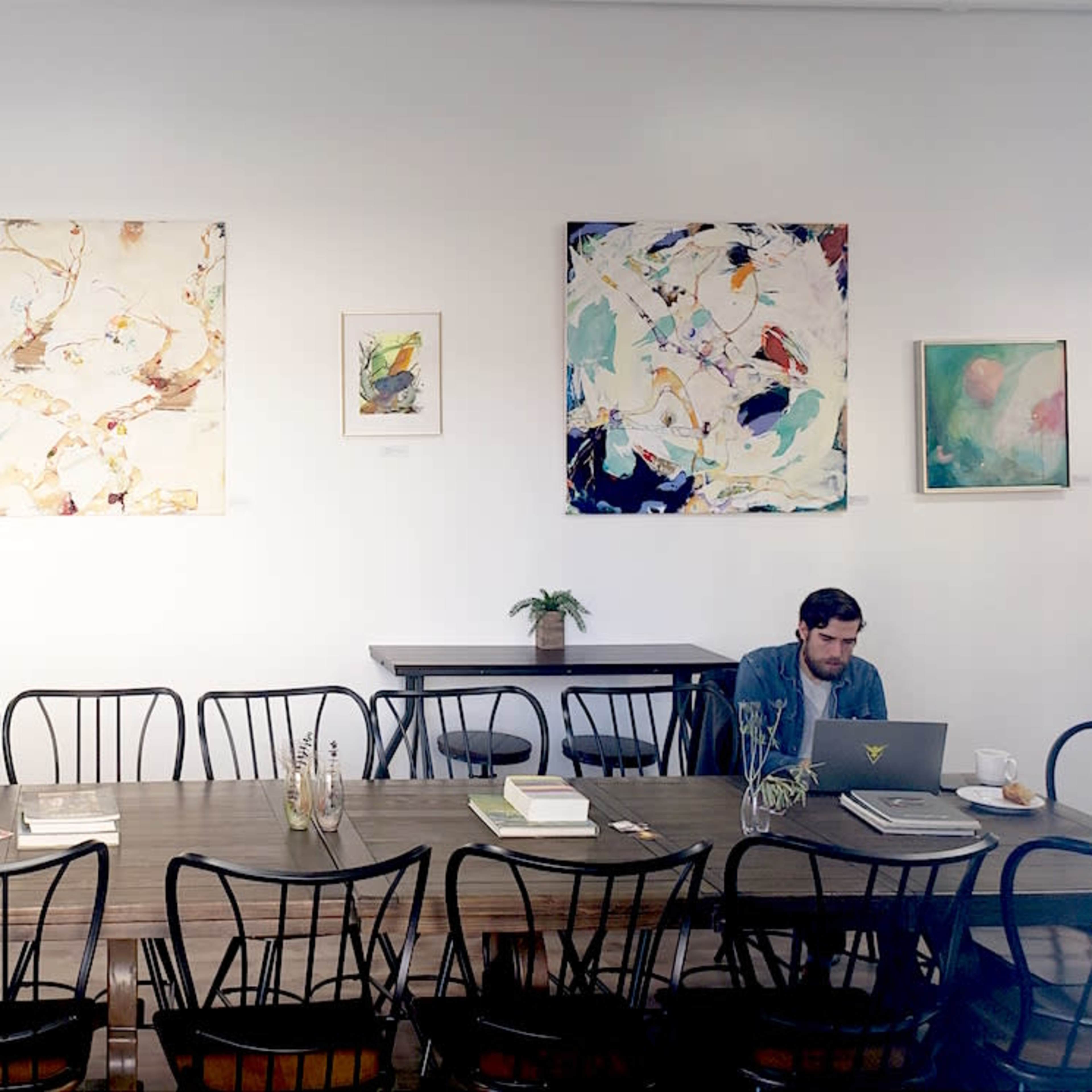 A long wooden table with black chairs occupies the center of a bright room adorned with various pieces of abstract art on the white walls.