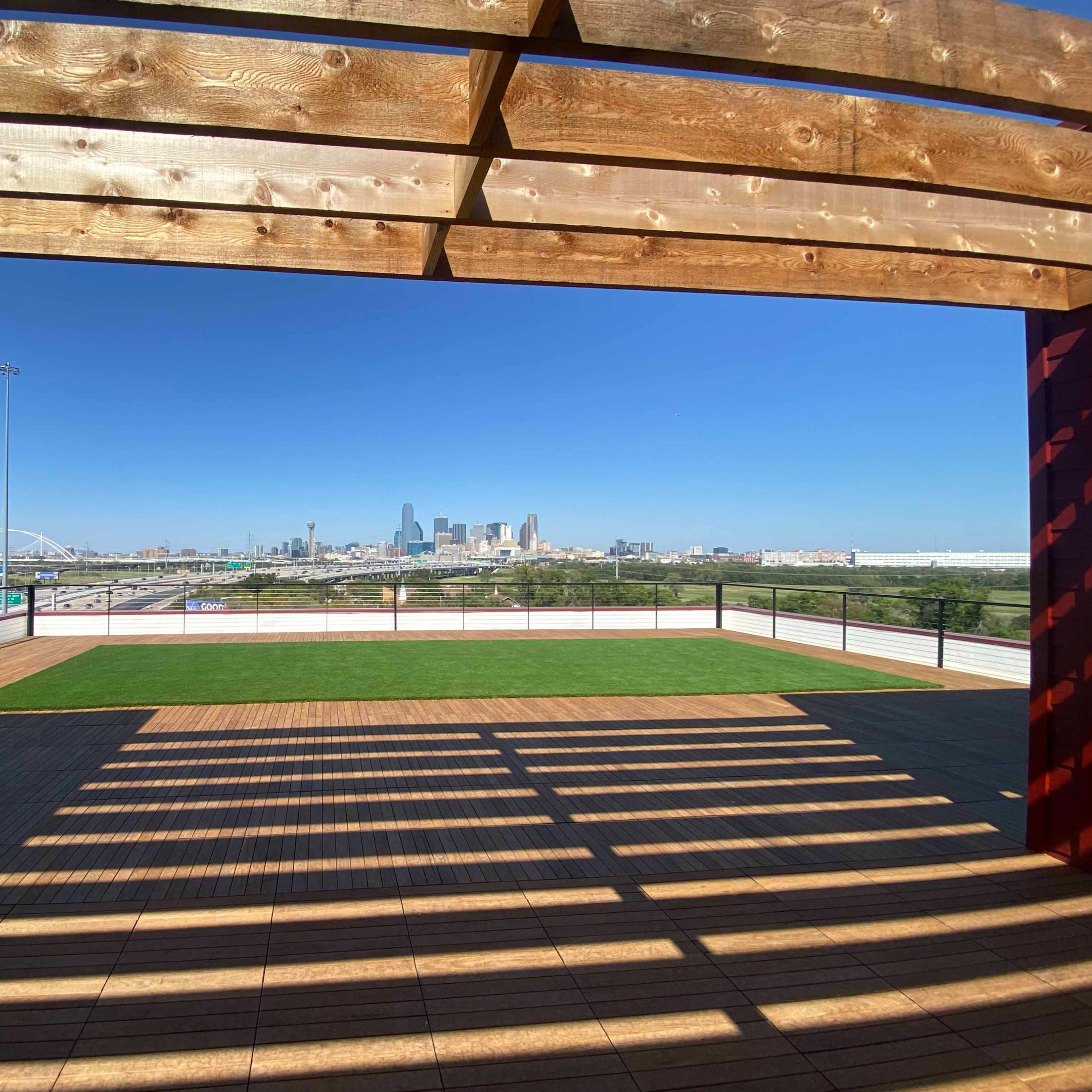 A rooftop terrace features wooden beams and a view of a city skyline with a clear blue sky.