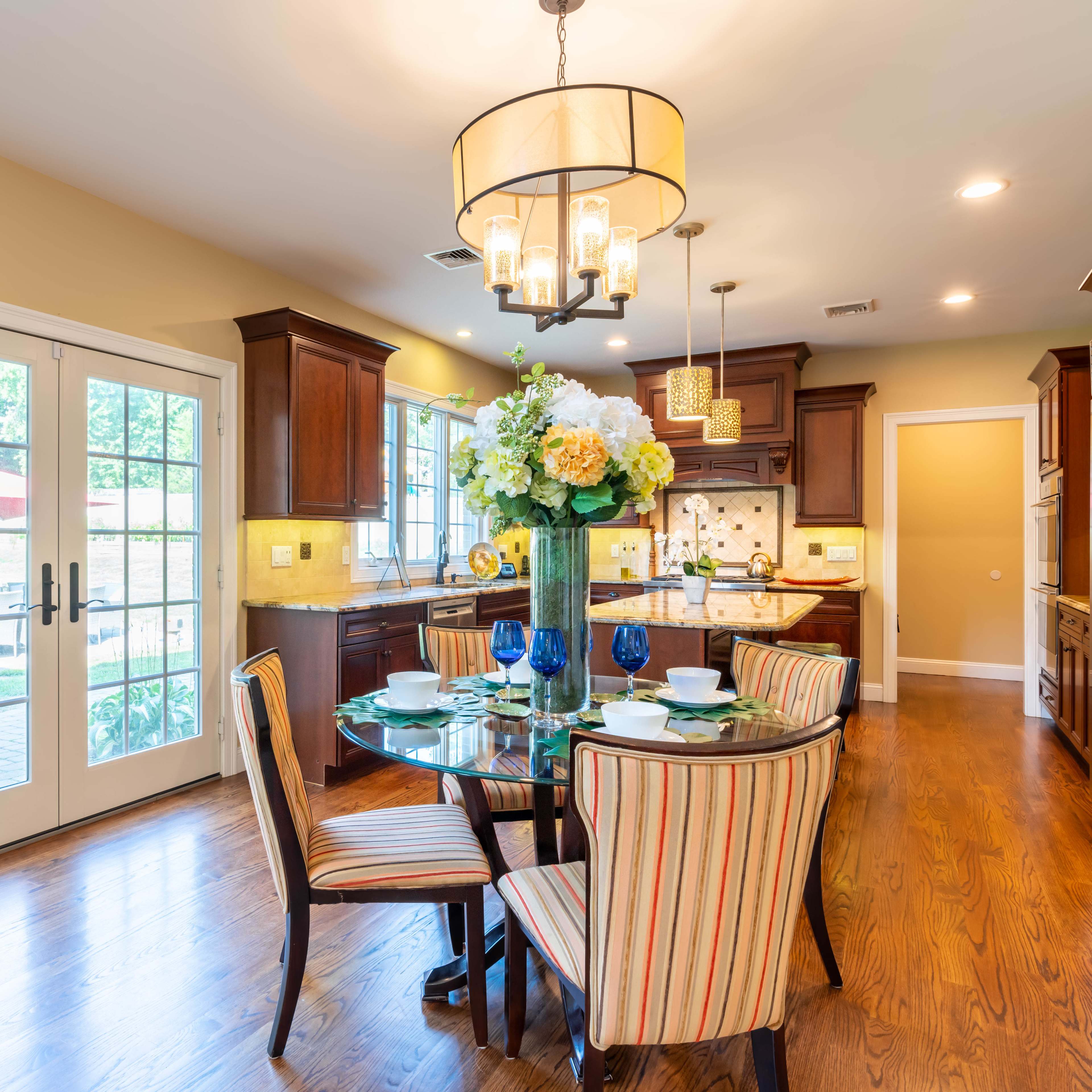 A kitchen with dark wood cabinets, a round dining table set for four, and large sliding glass doors leading to an outdoor area.