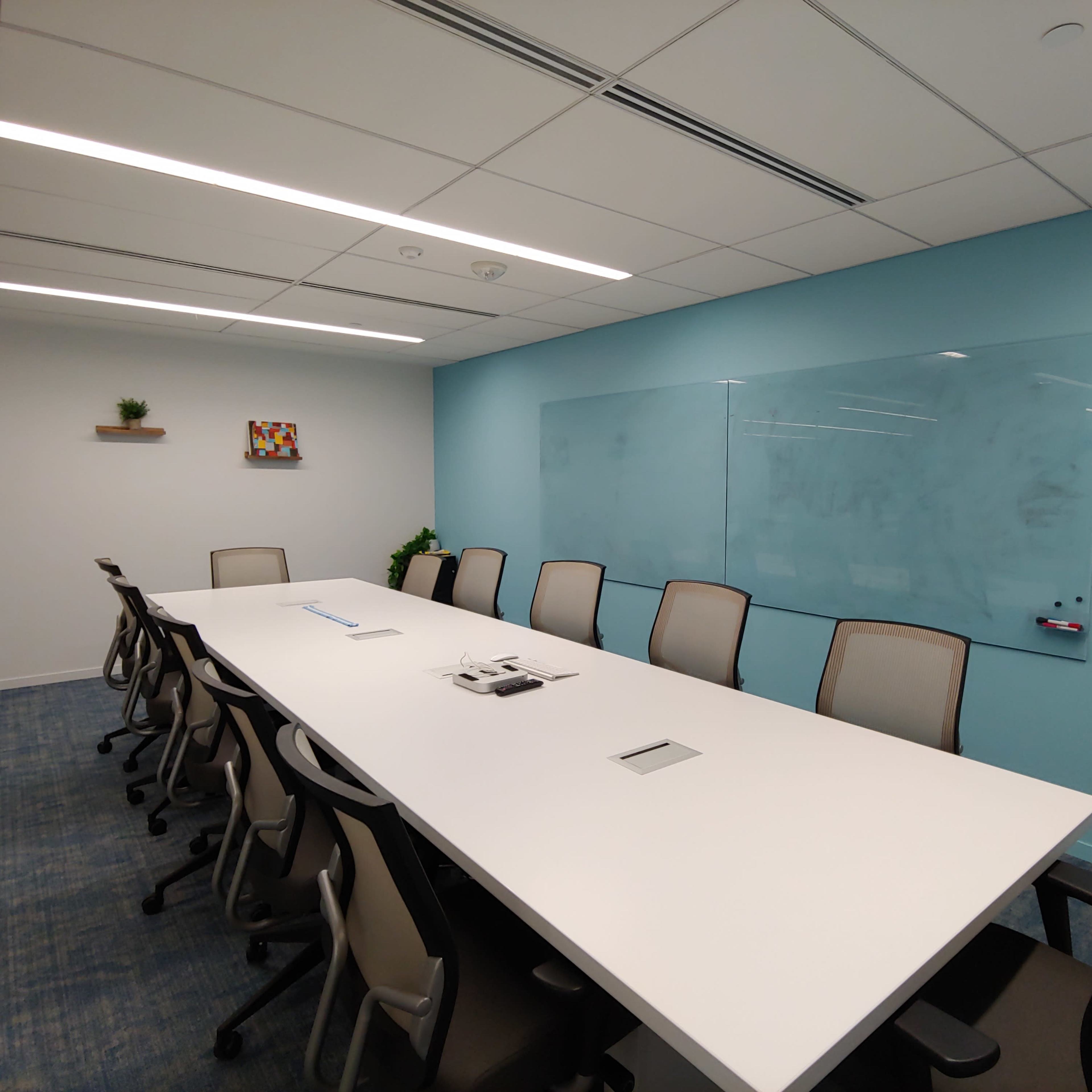 A modern conference room with a long white table, ergonomic chairs, and a blue accent wall featuring a clear whiteboard.
