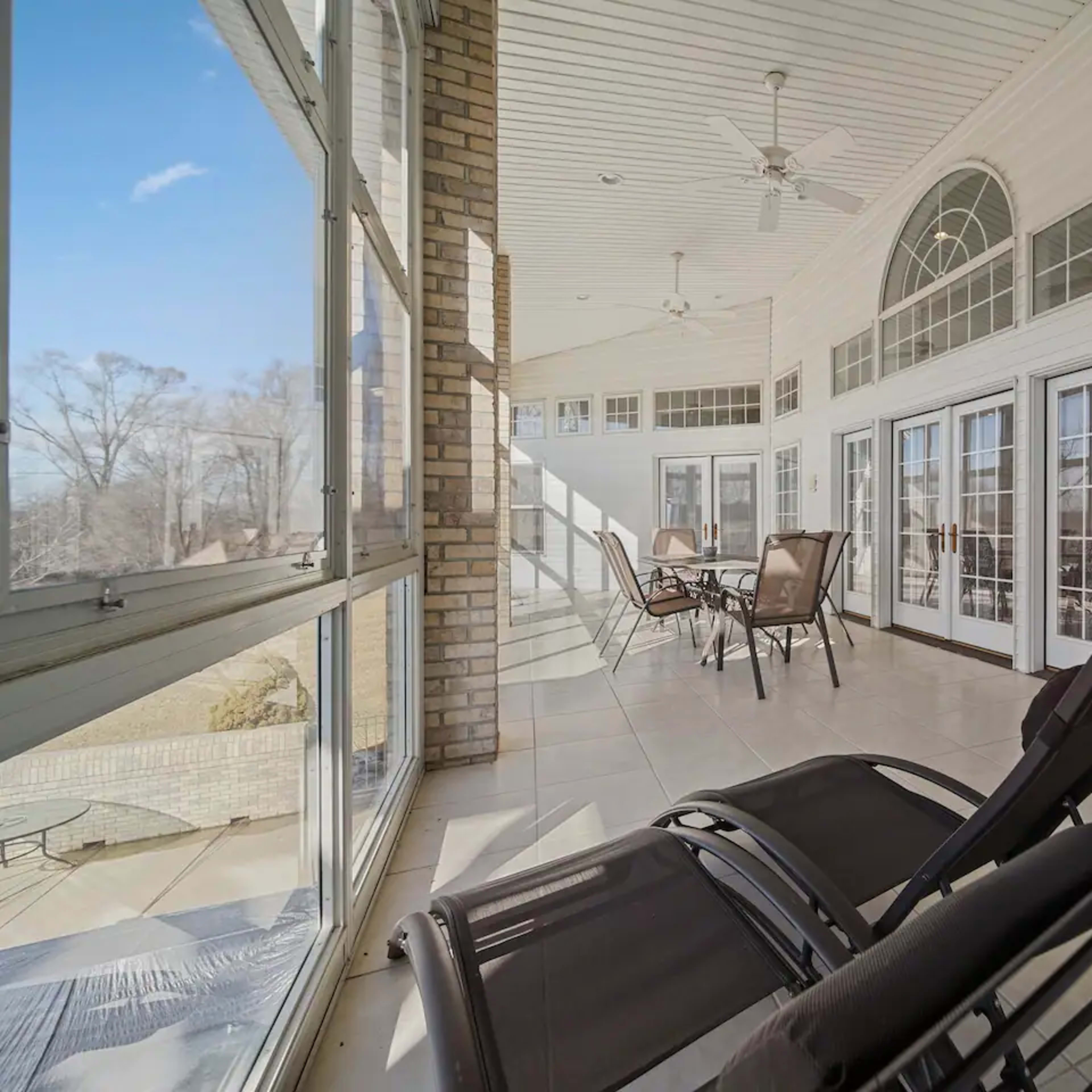 A spacious sunroom with large windows, providing ample natural light, and featuring several chairs arranged around a table.