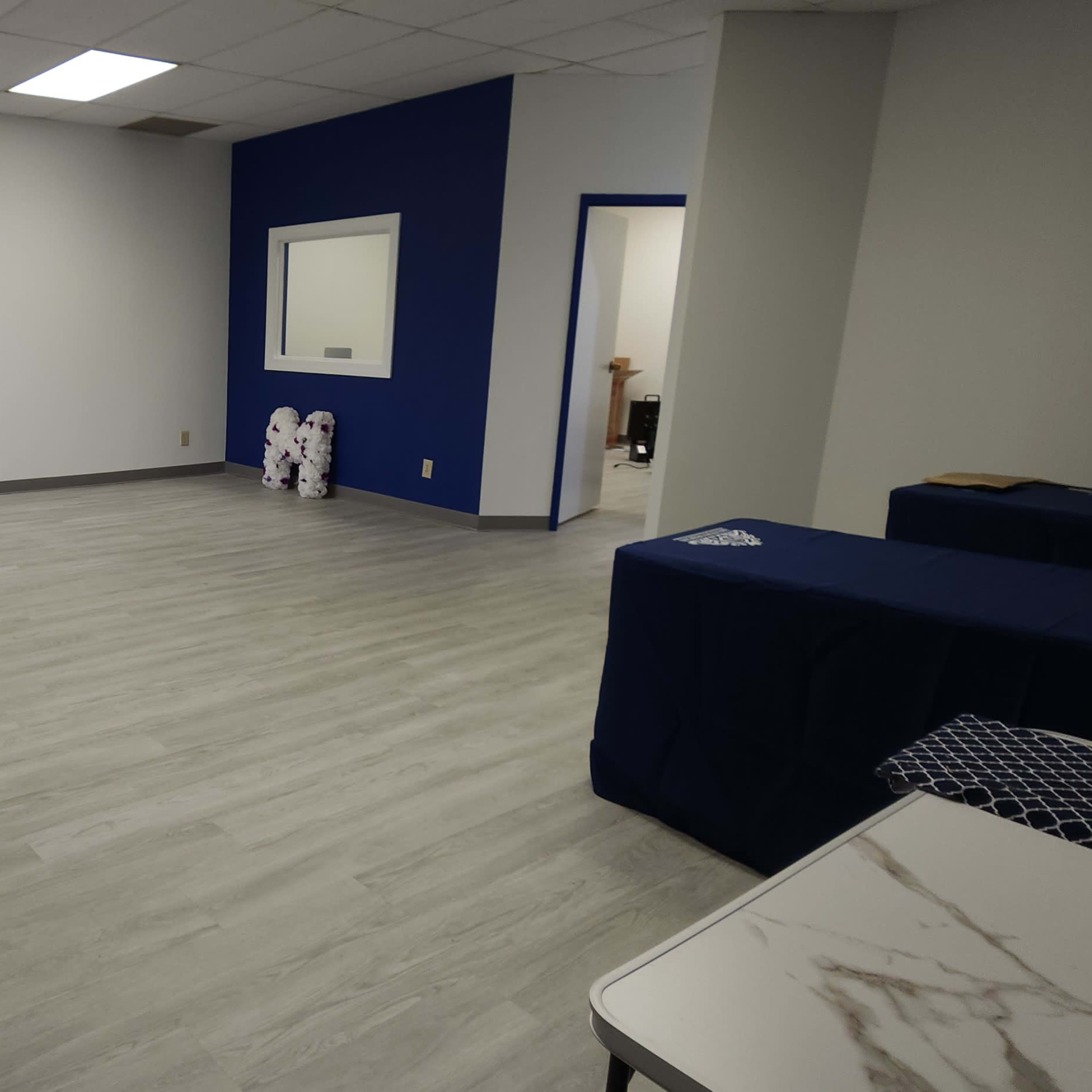 A spacious, empty interior room with light gray flooring, blue accent walls, and minimal furniture.