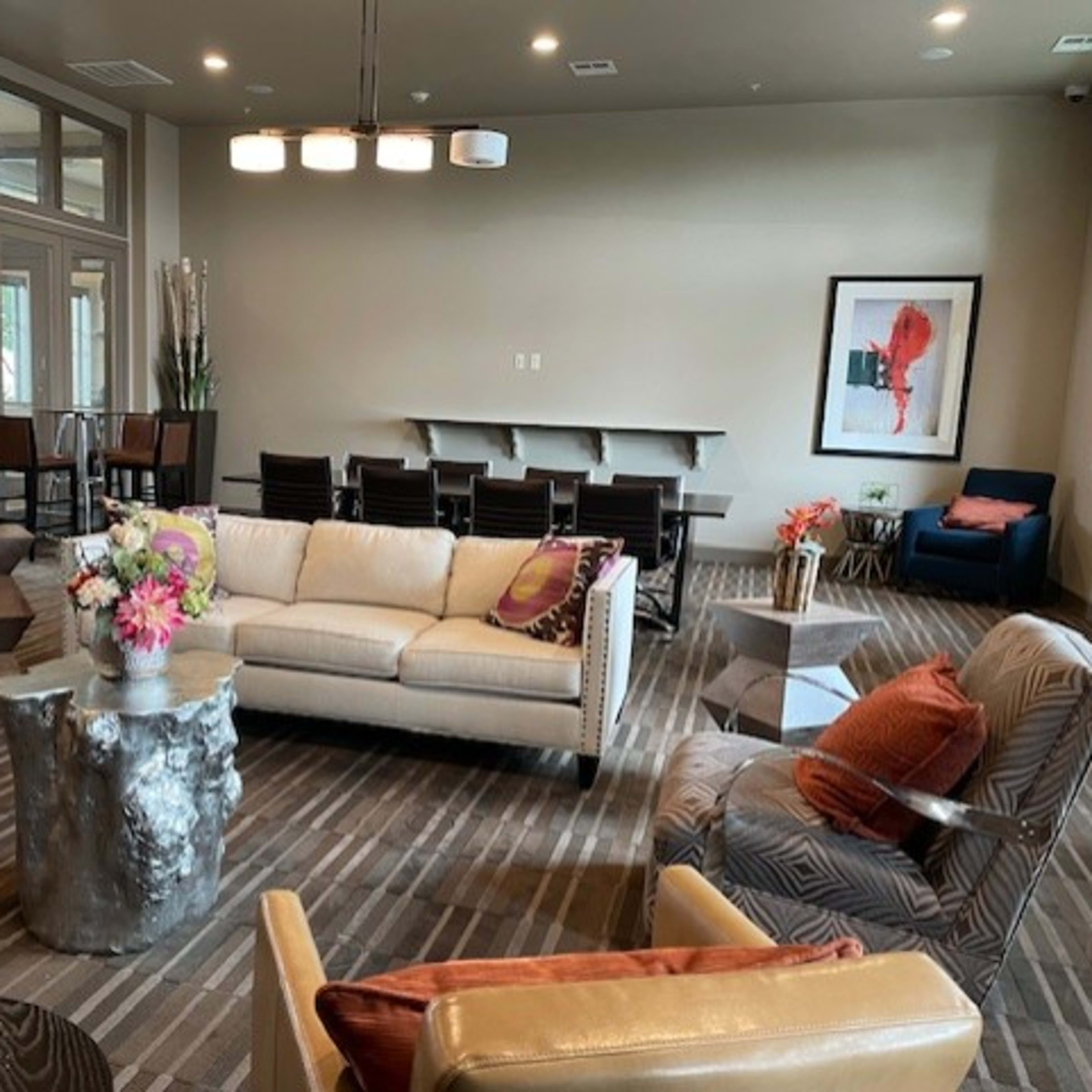 A modern lounge area with a cream-colored sofa, several patterned armchairs, a coffee table, and a dining area with a long table in the background.