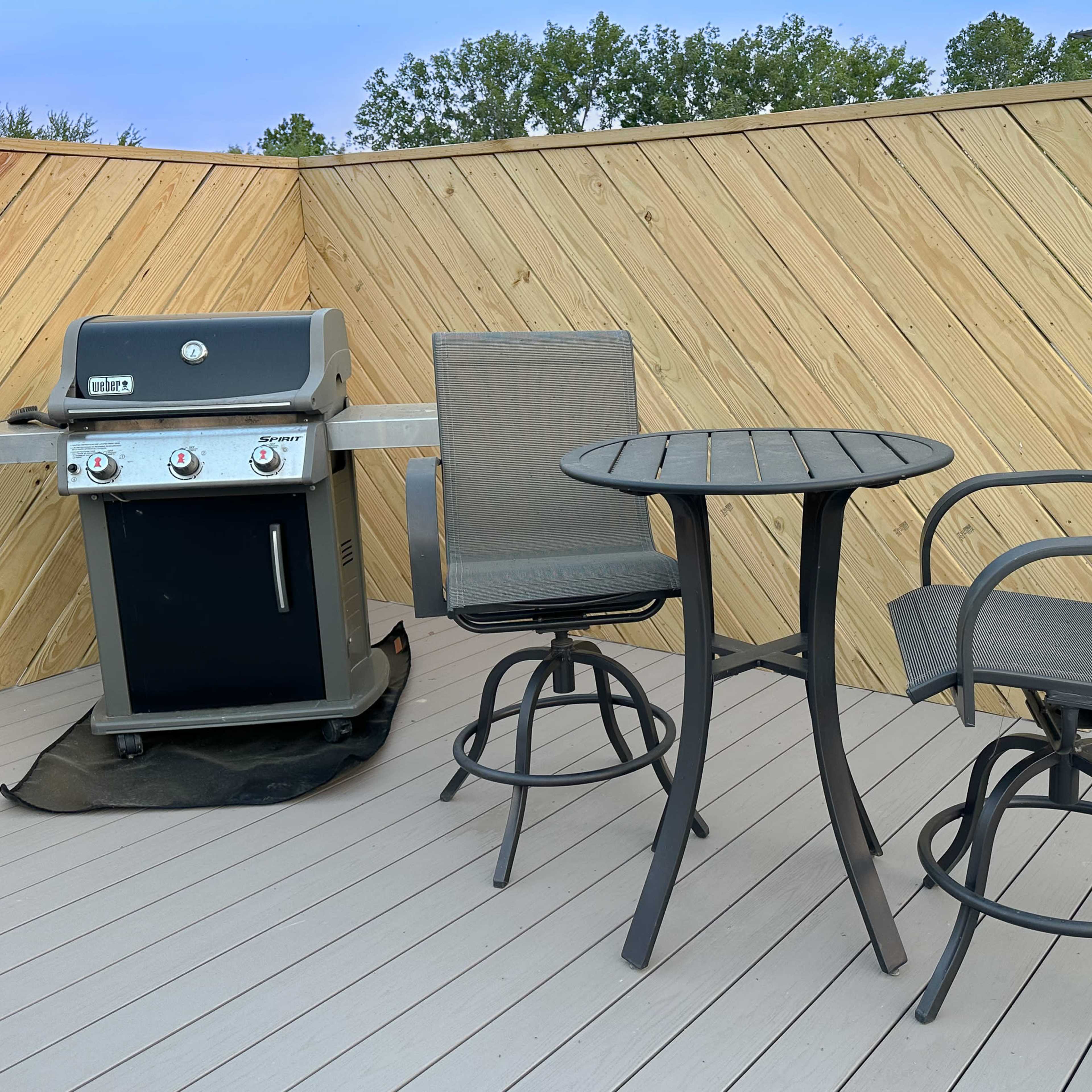 A small outdoor patio area with a grill, a round table, and two high-backed chairs.