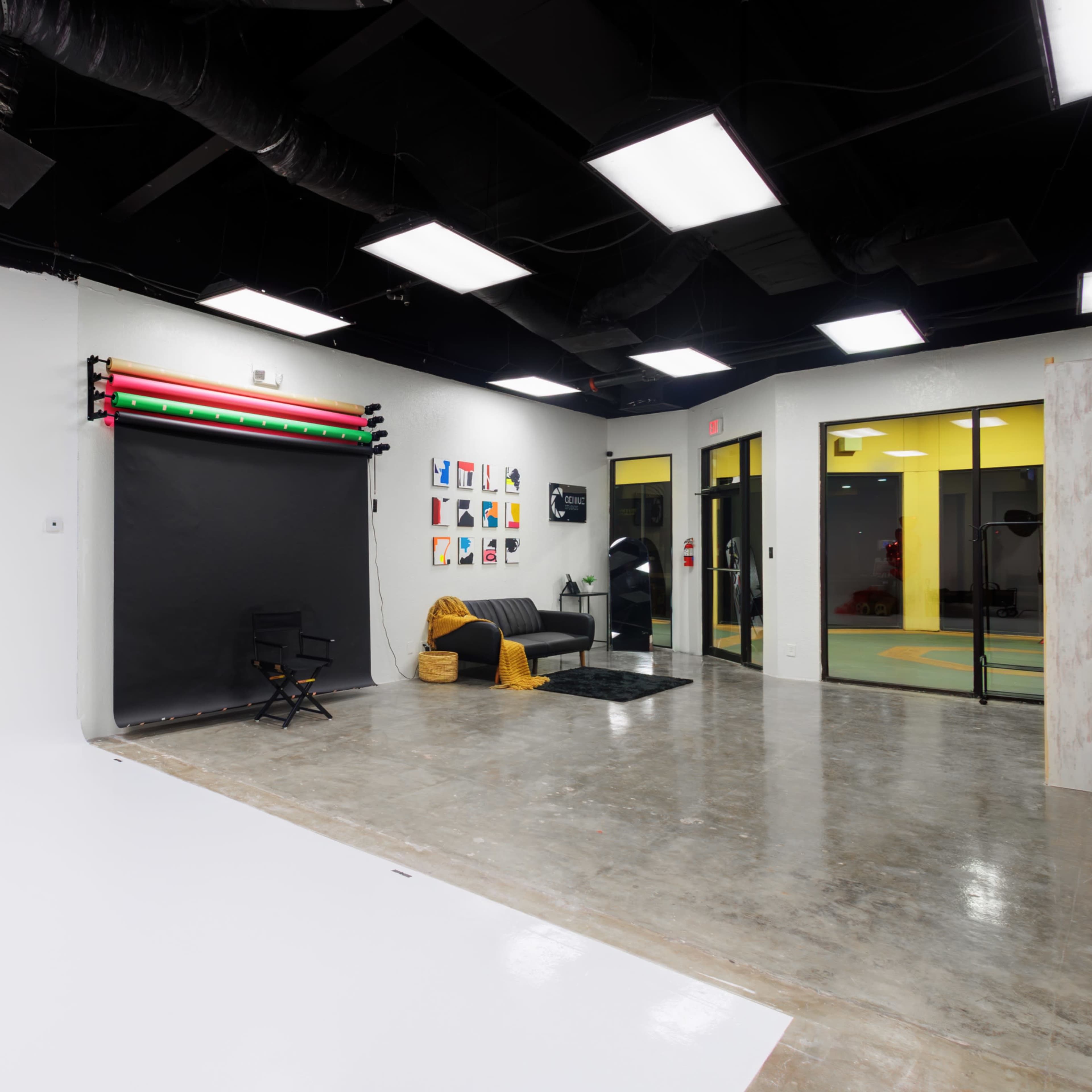A spacious photography studio with a black backdrop, a seating area, and various colorful artworks displayed on the wall.