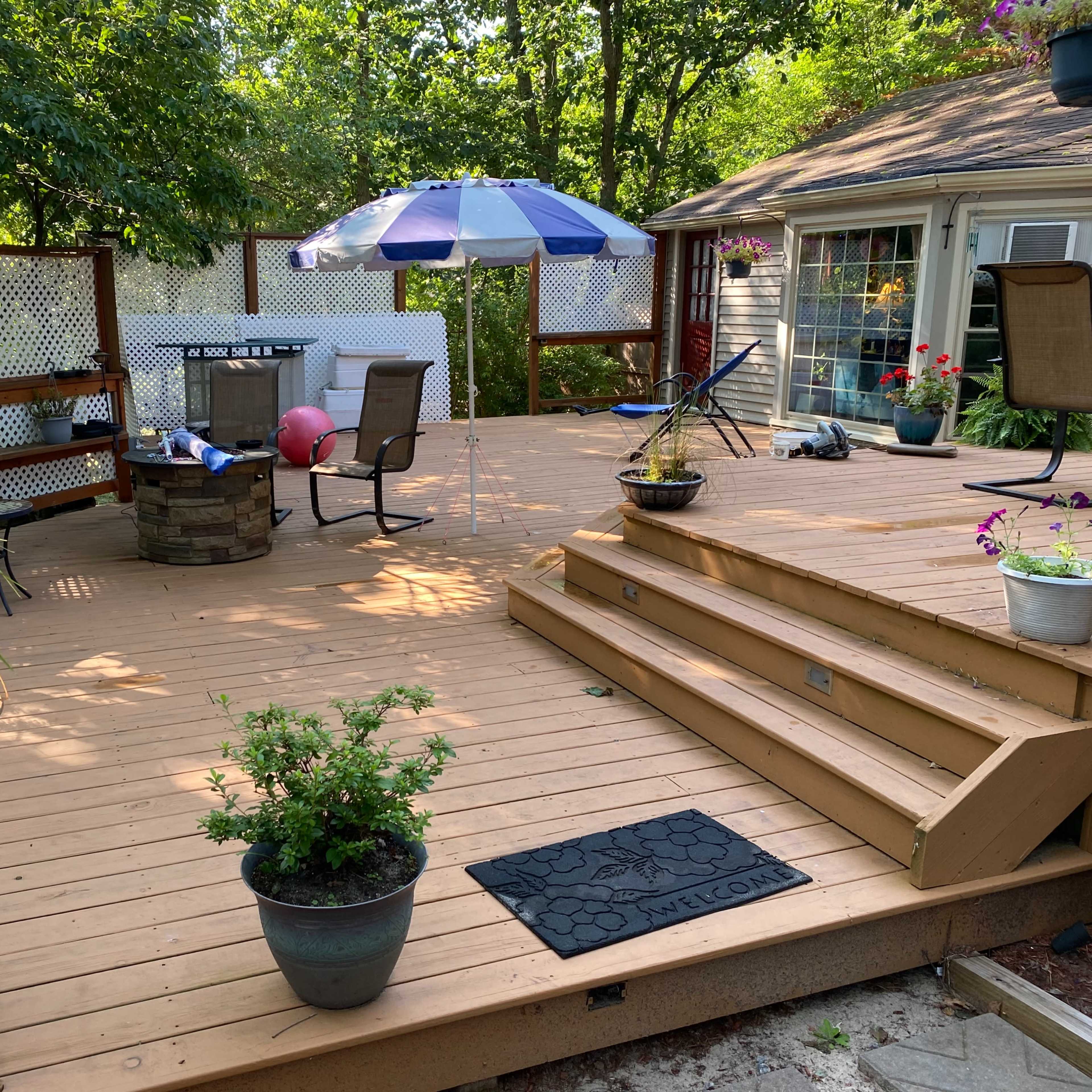 A wooden deck with a table and chairs, an umbrella, and potted plants arranged around the area.