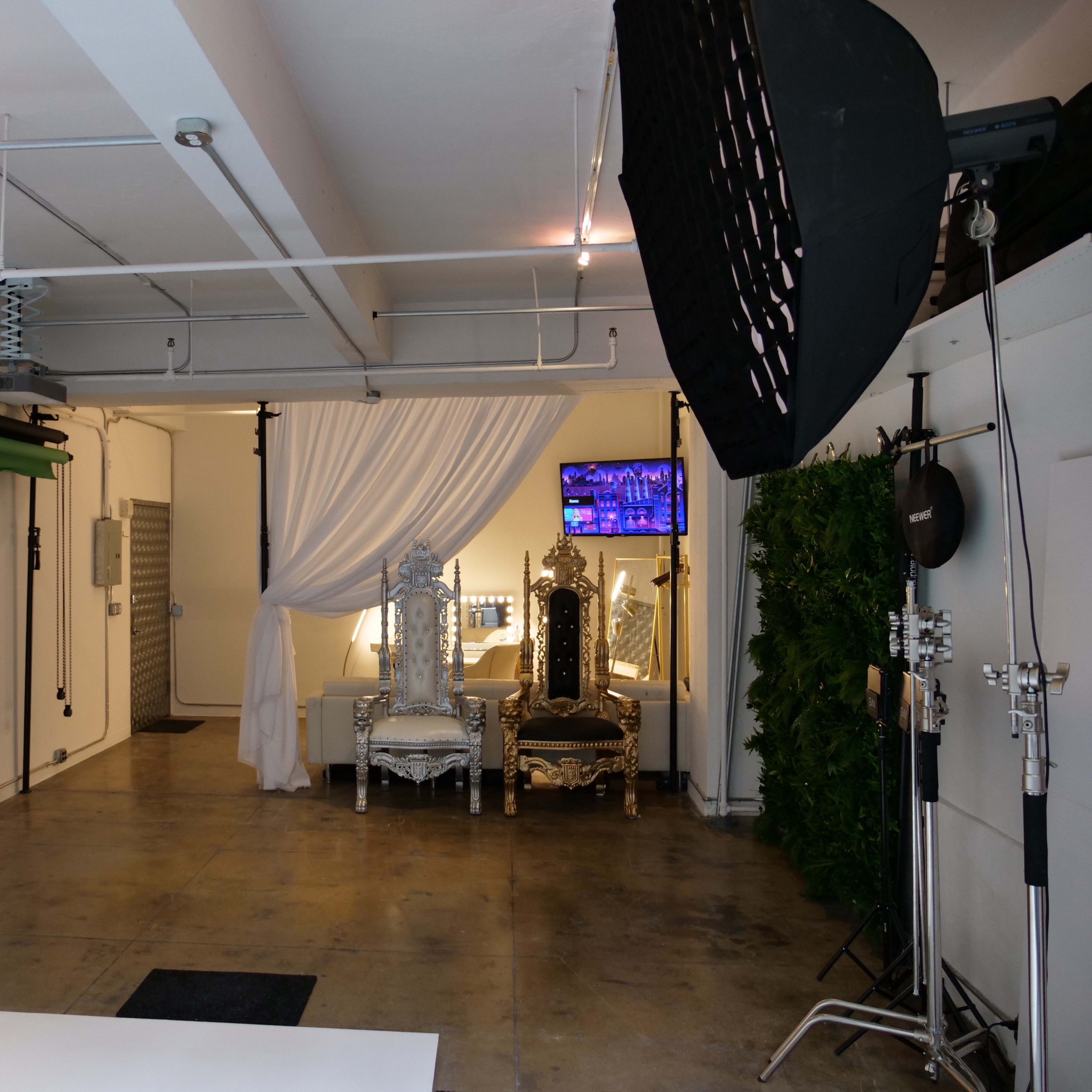 A photography studio featuring two ornate chairs, soft lighting, and various photography equipment set up in a spacious area.