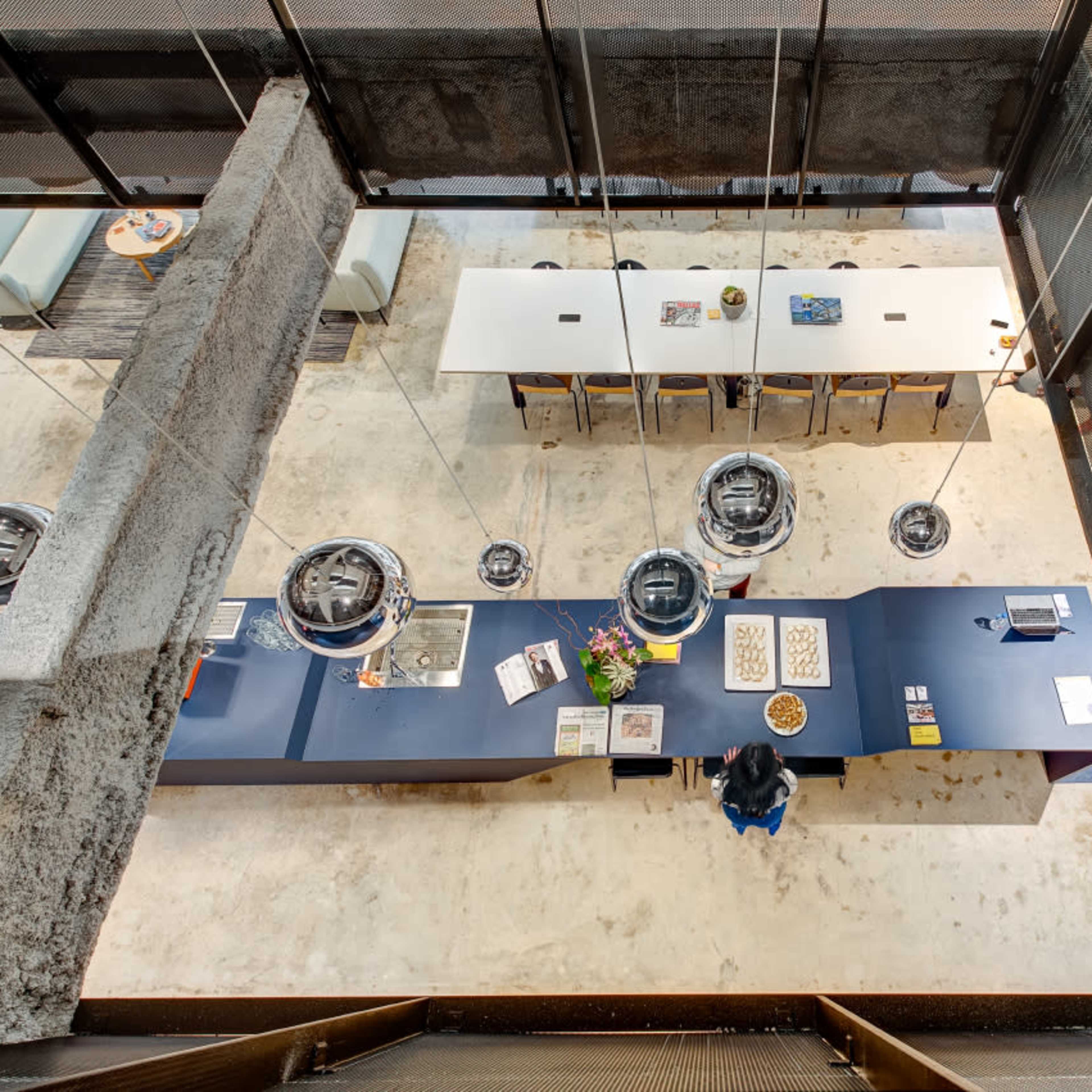 A modern office interior with a central reception desk, surrounded by tables and chairs, under a multi-level architectural design.