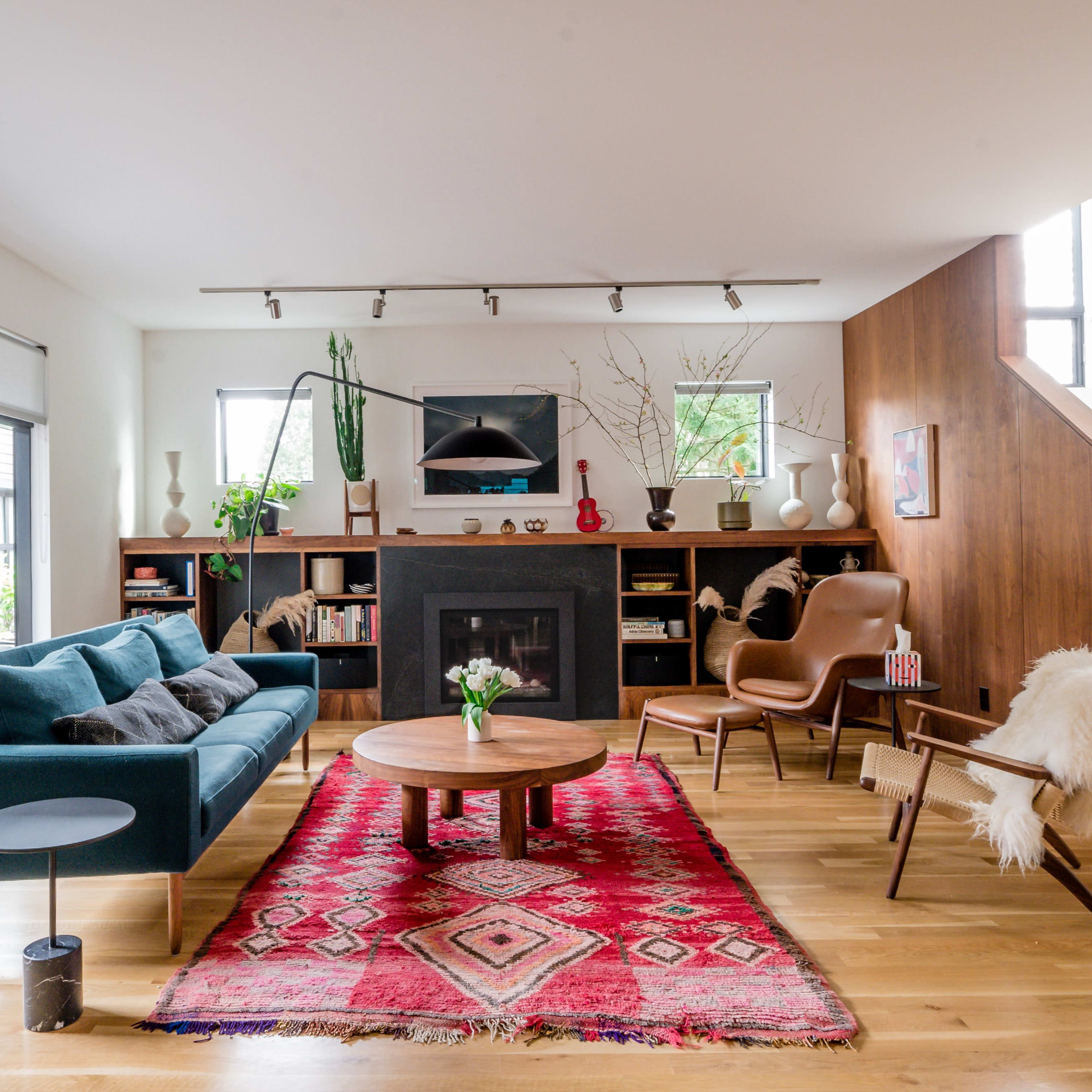 The living room features a teal sofa, a round wooden coffee table, a large area rug, and a staircase leading to the upper level.