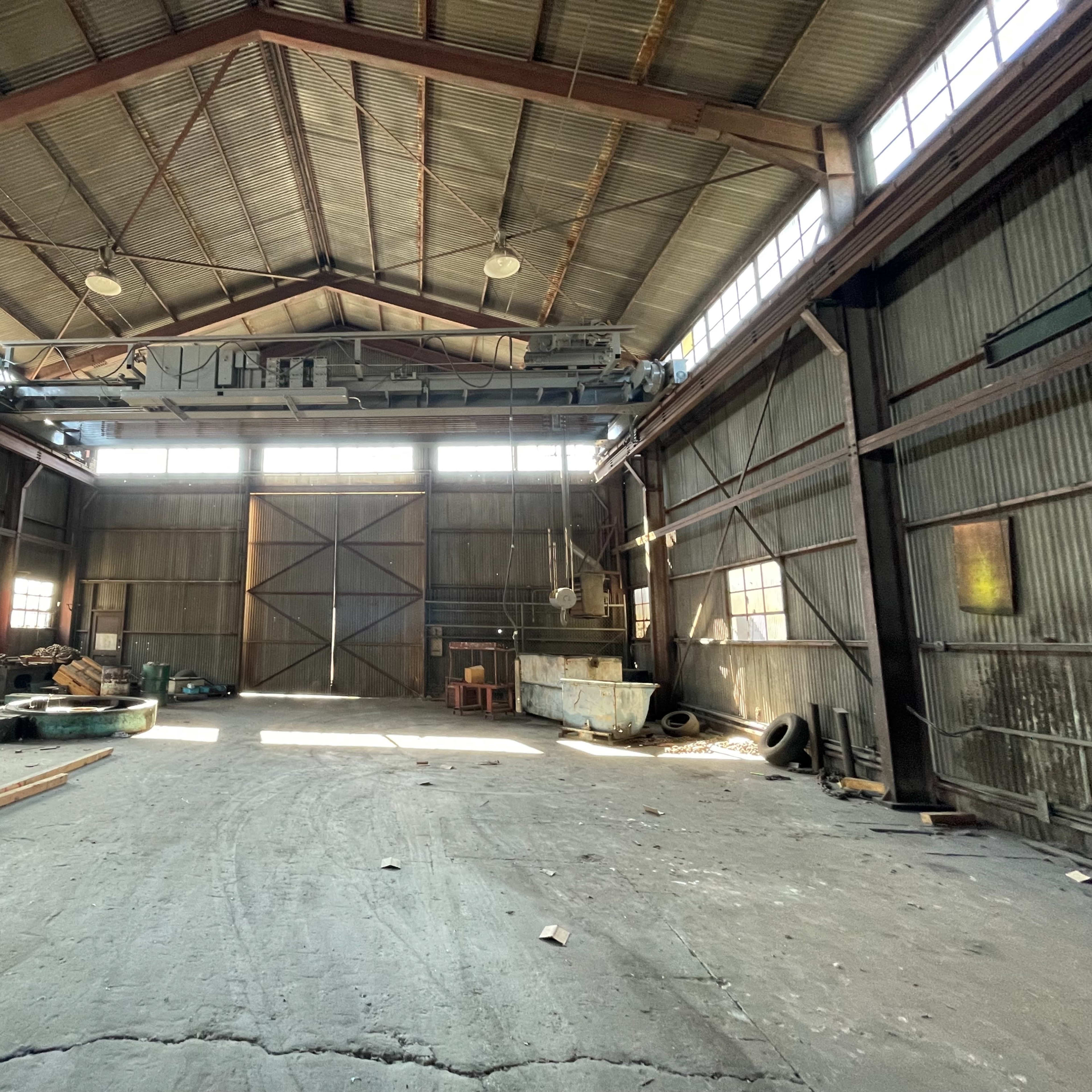 The interior of a large industrial warehouse features high ceilings, exposed beams, and scattered construction materials.